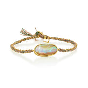 A gold-plated braided bracelet featuring a central oval iridescent opal stone and a small tassel detail, shown on a clean white background.