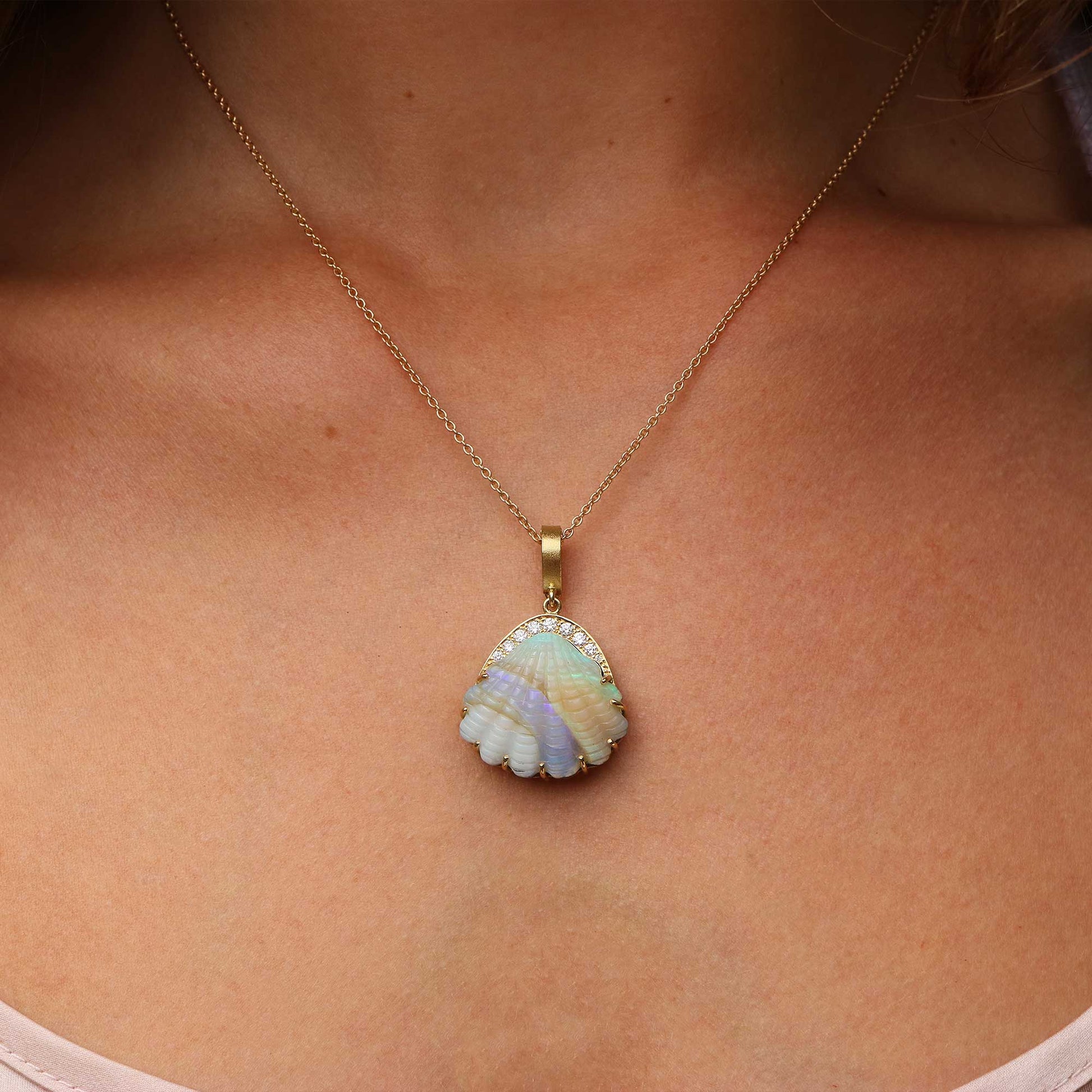 A gold chain necklace with a scallop-shaped pendant featuring iridescent opal shell-like segments in pale blue, lavender, and cream, bordered by small diamond stones, shown worn on a model's neck.