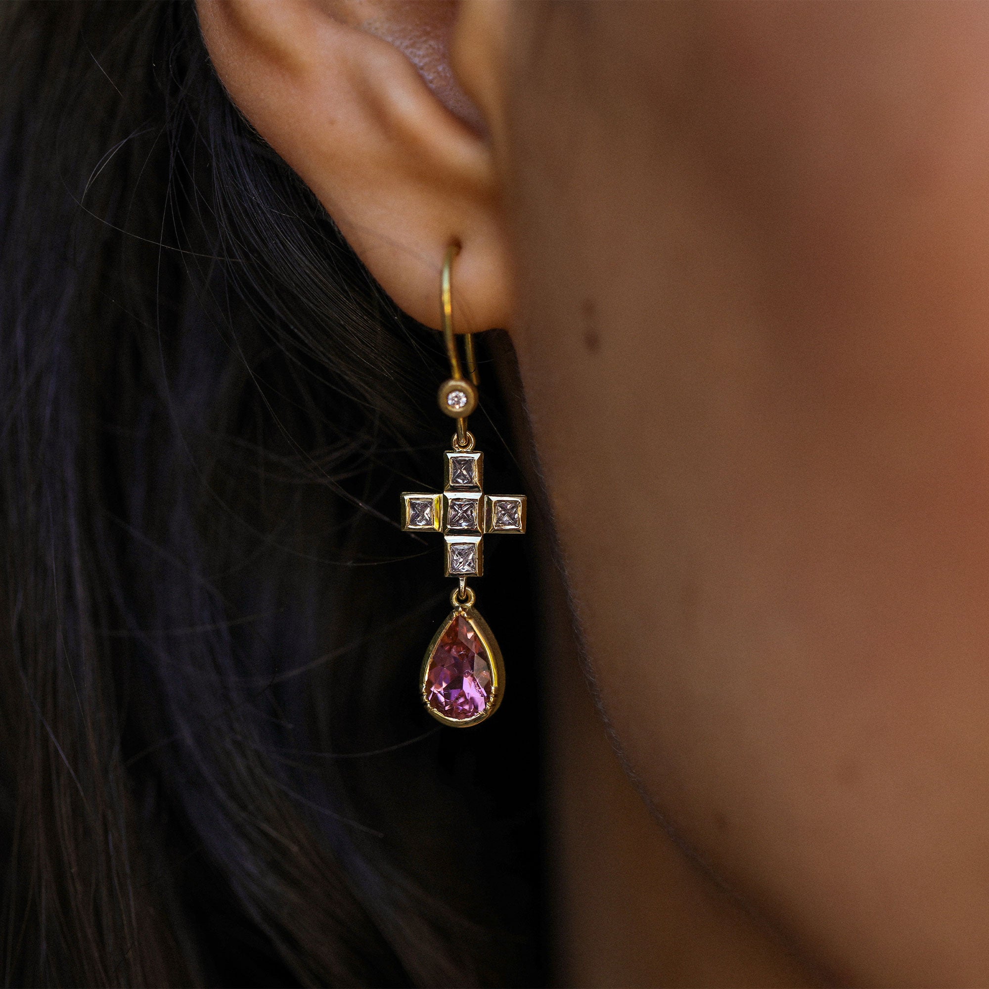 Close-up of a person wearing a gold earring with pink tourmalines and white diamonds by Brooke Gregson.