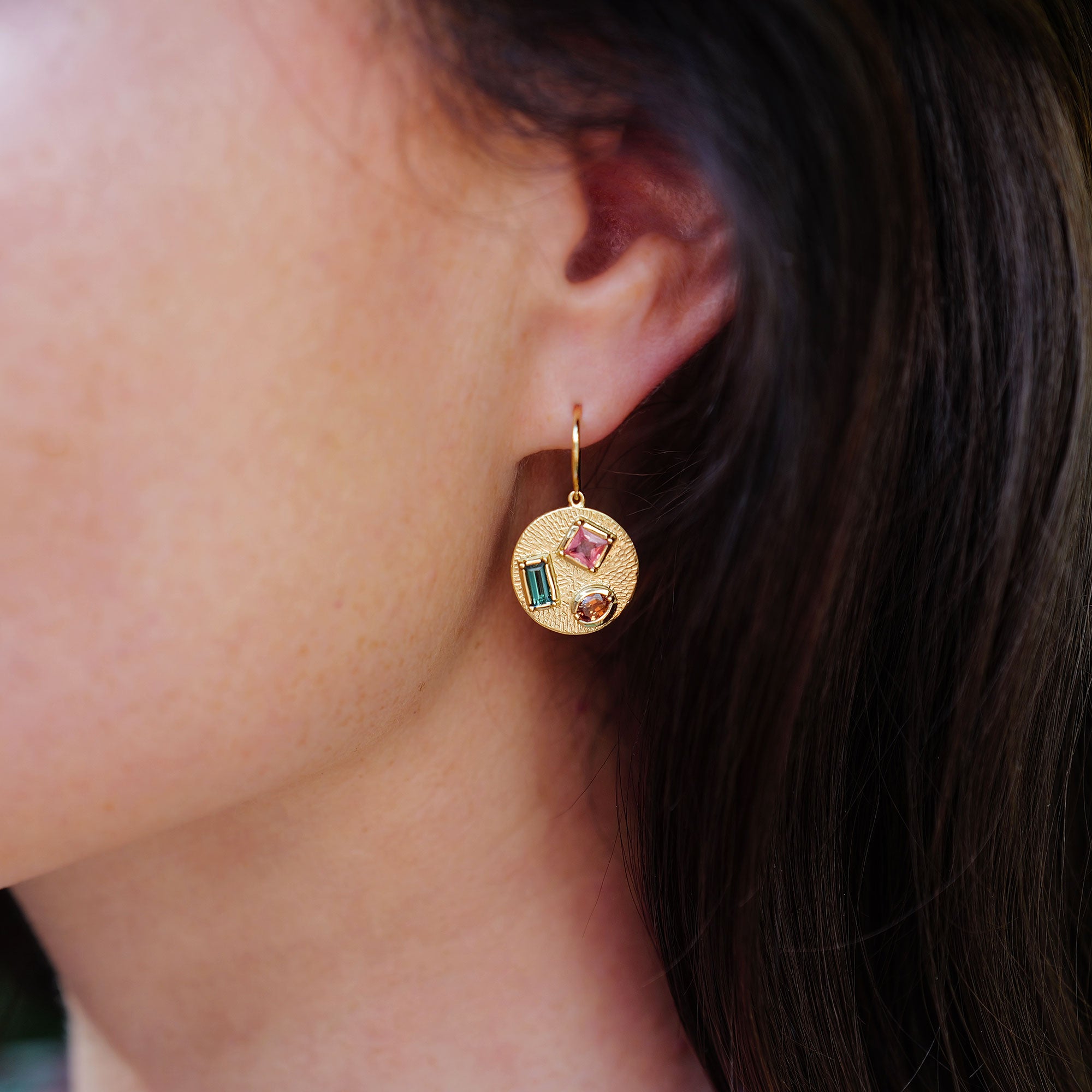 Close up of girl wearing 18k gold earrings with hand engraving and mixed sapphires by Brooke Gregson.