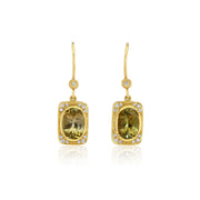 A pair of gold drop earrings featuring rectangular yellow-green tourmline gemstones surrounded by small diamond stones, shown on a clean white background with a soft reflection below.