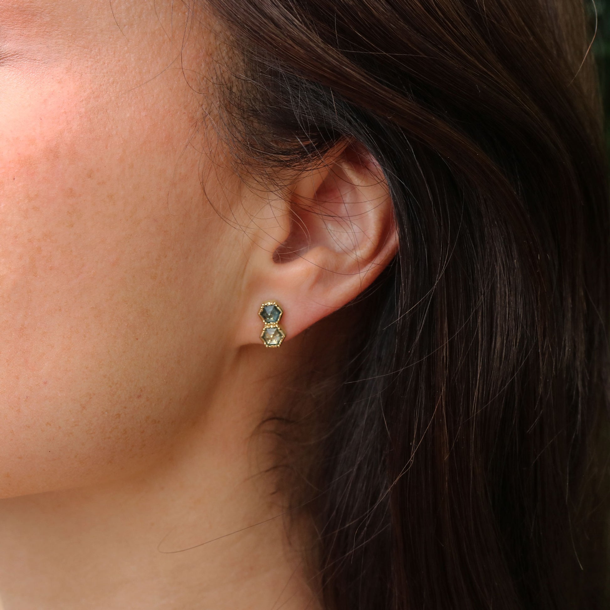 Close-up of an ear wearing a gold earring with montana sapphire gemstones.