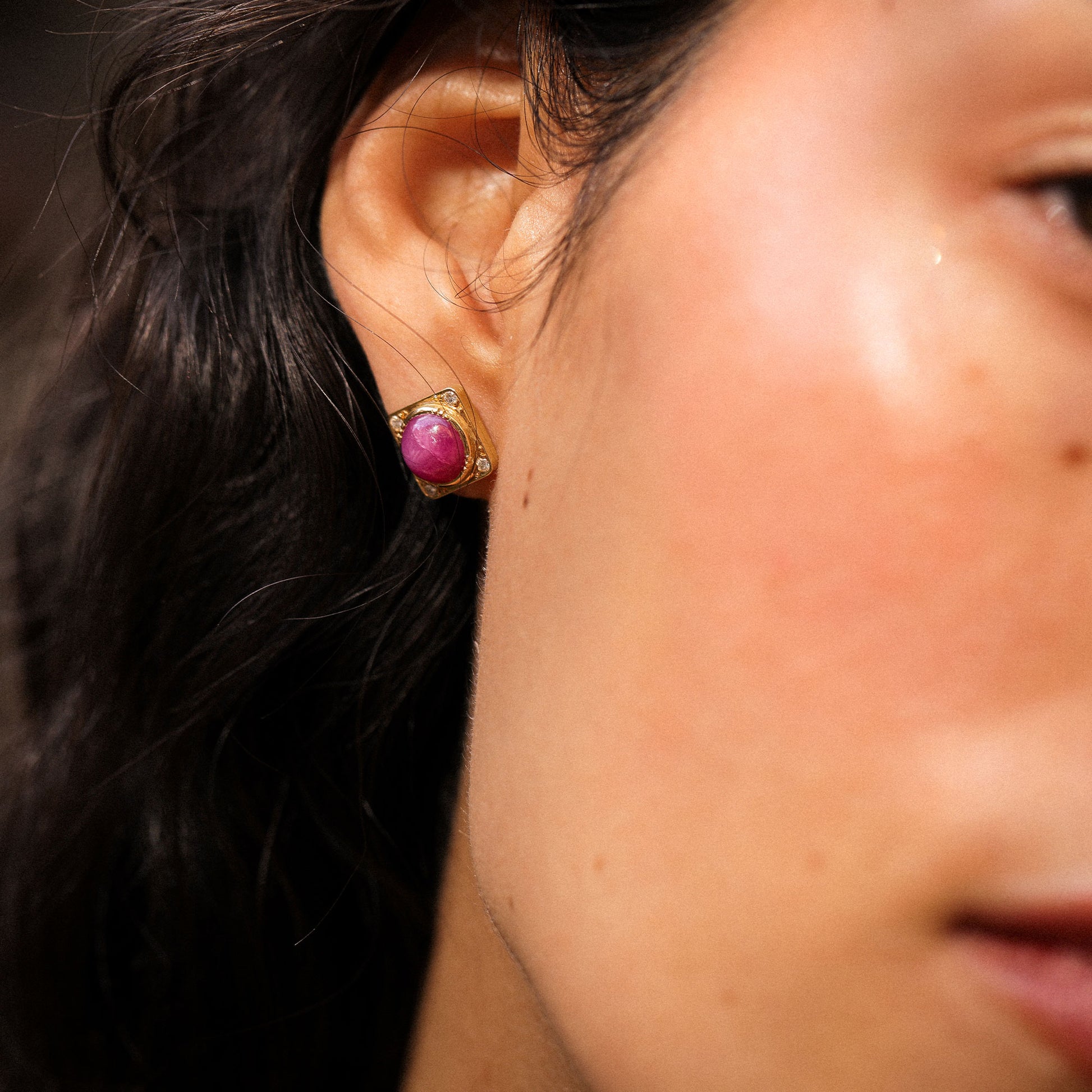 Close-up of an ear wearing a gold earring with a ruby gemstone by designer Brooke Gregson.