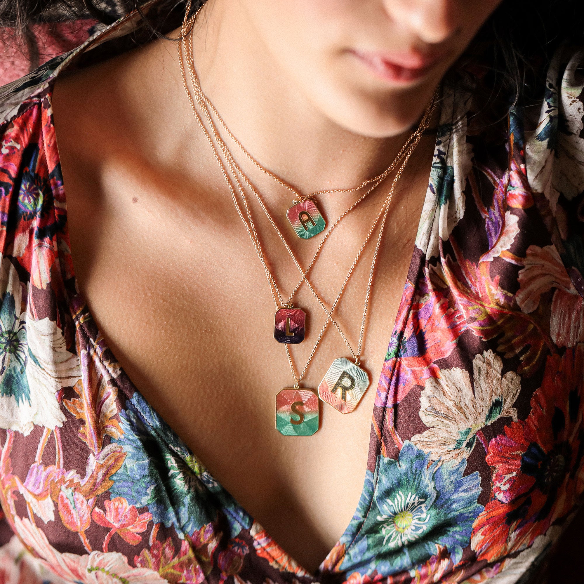 Necklace with colorful pendant letters worn by a person in a floral top