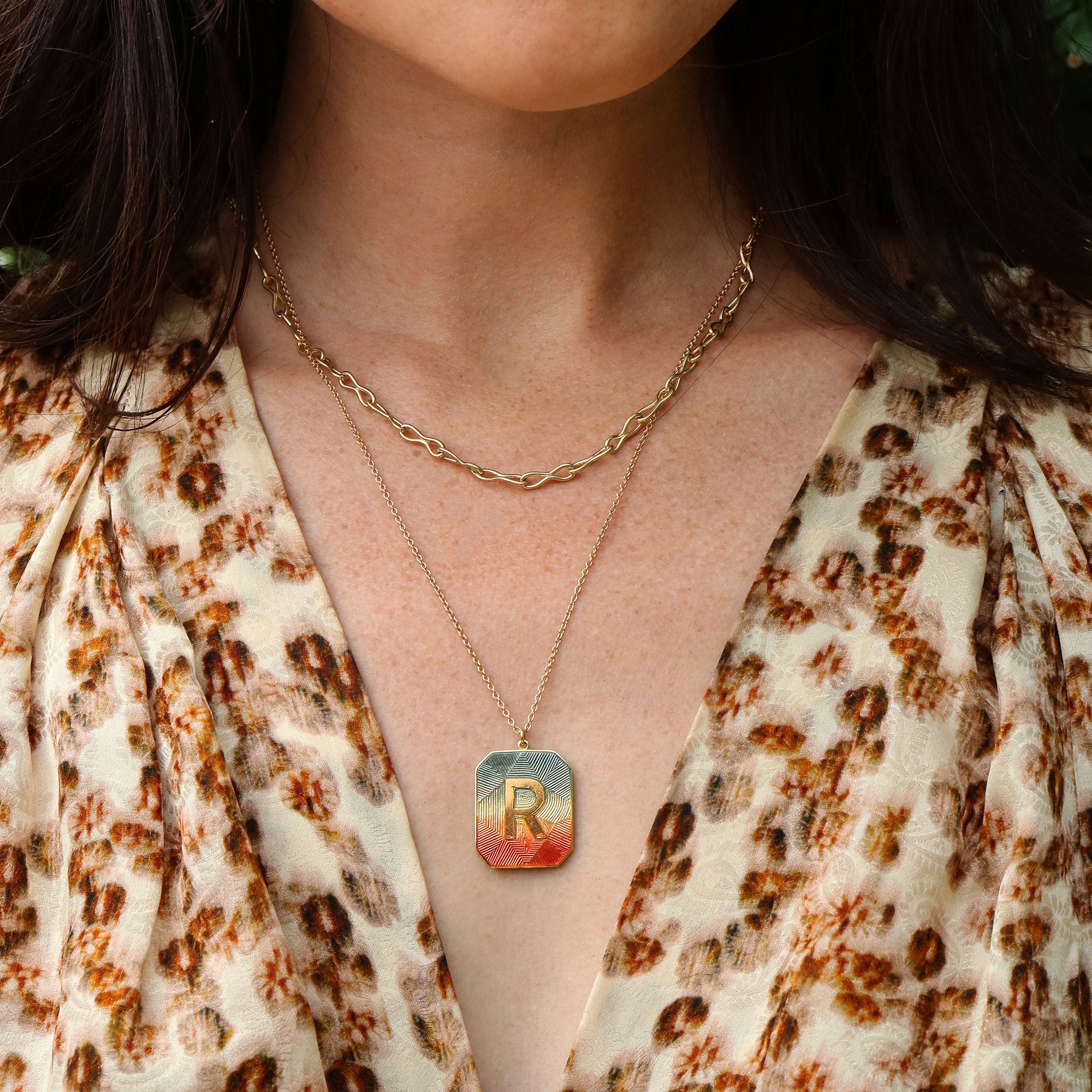 Necklace with an enamel pendant featuring the letter 'R' worn by a person in a floral top.