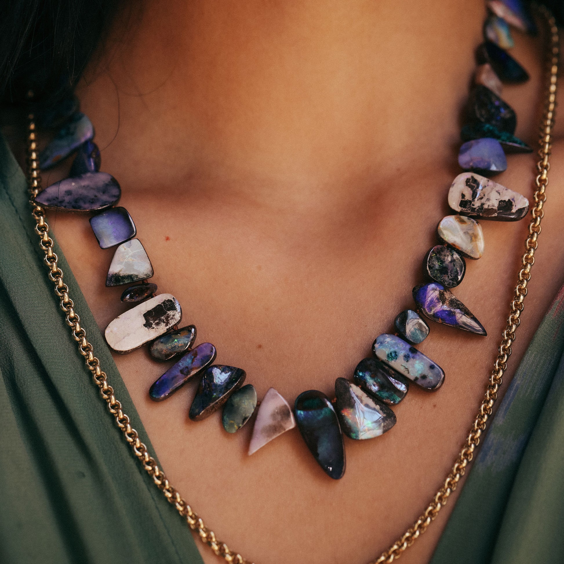 Necklace with multicolored stones and gold chain on a person wearing a green garment.