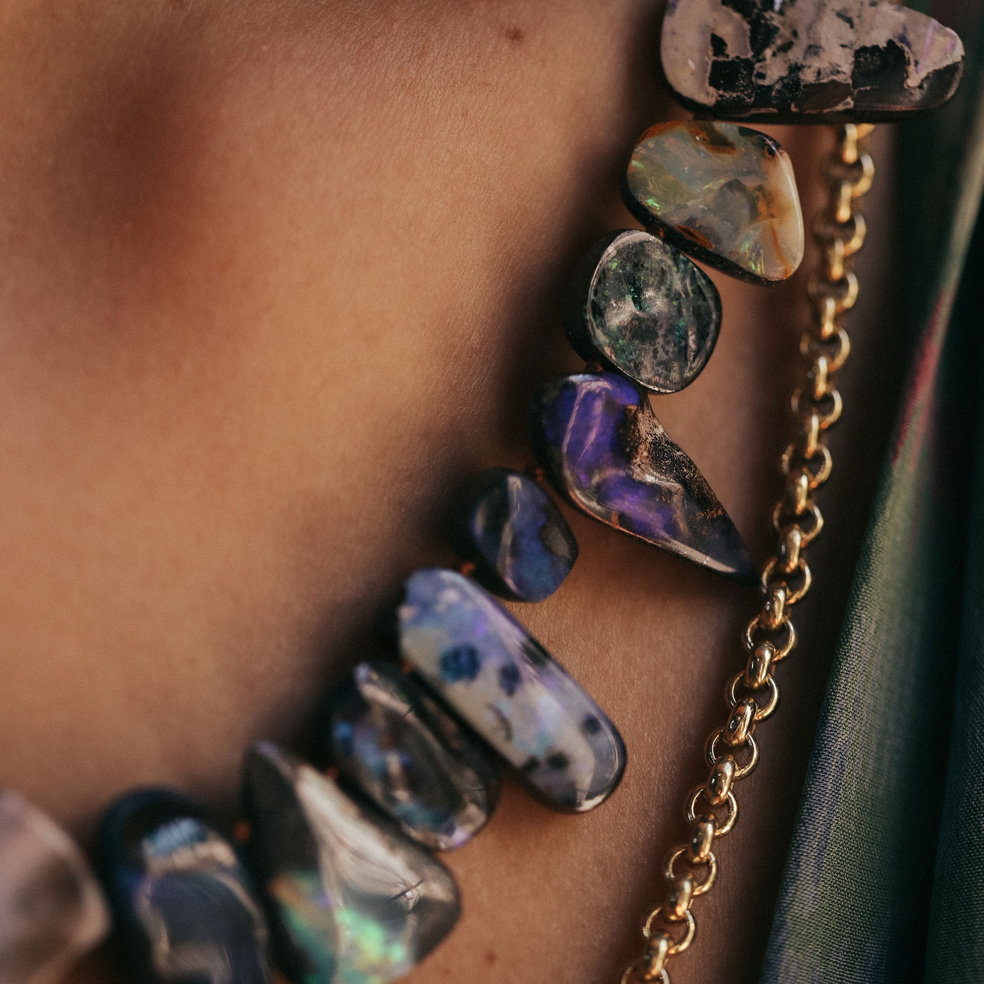 Close-up of a person wearing a necklace with multicolored stones and a gold chain.