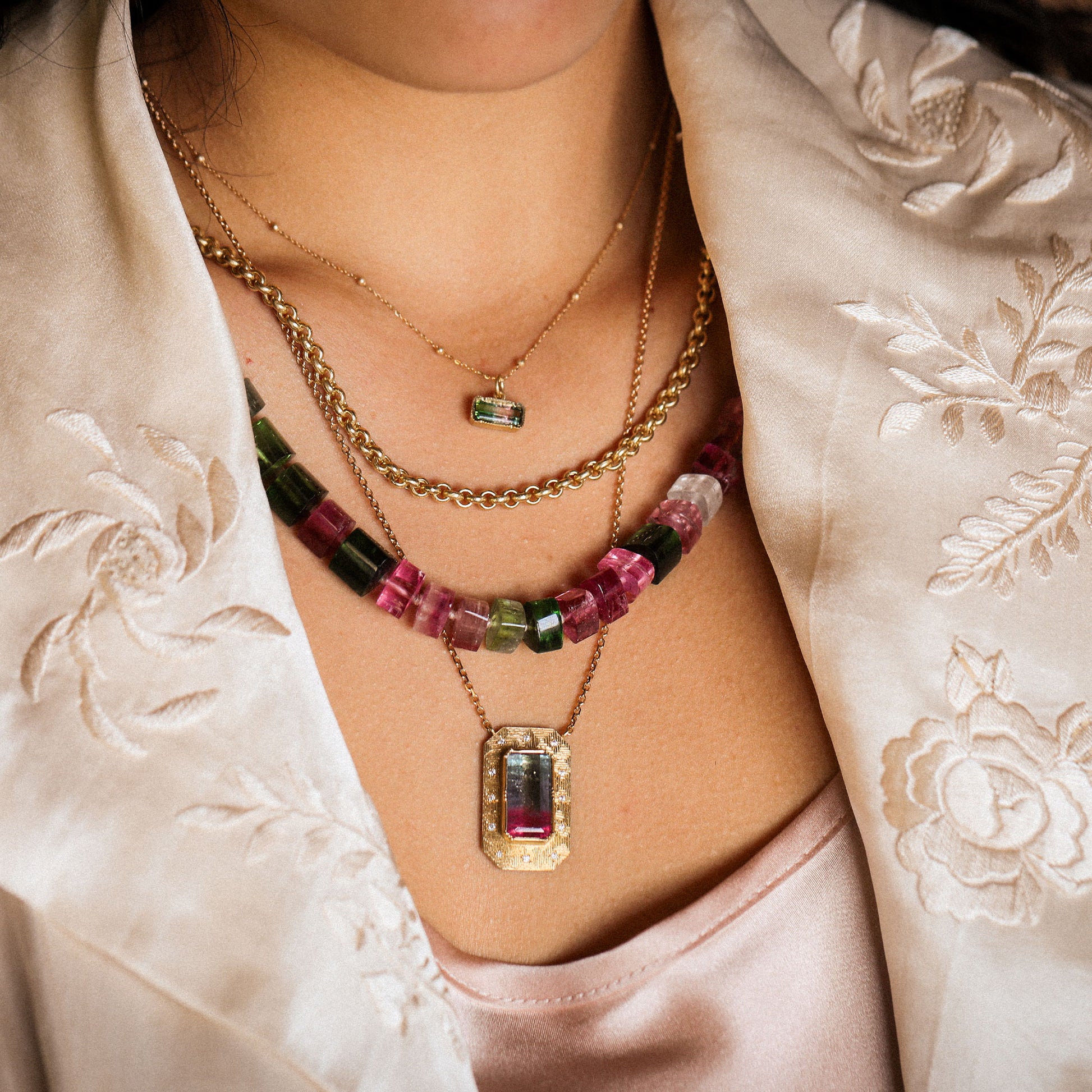 Close-up of a person wearing multiple necklaces with gemstones on a light-colored garment.