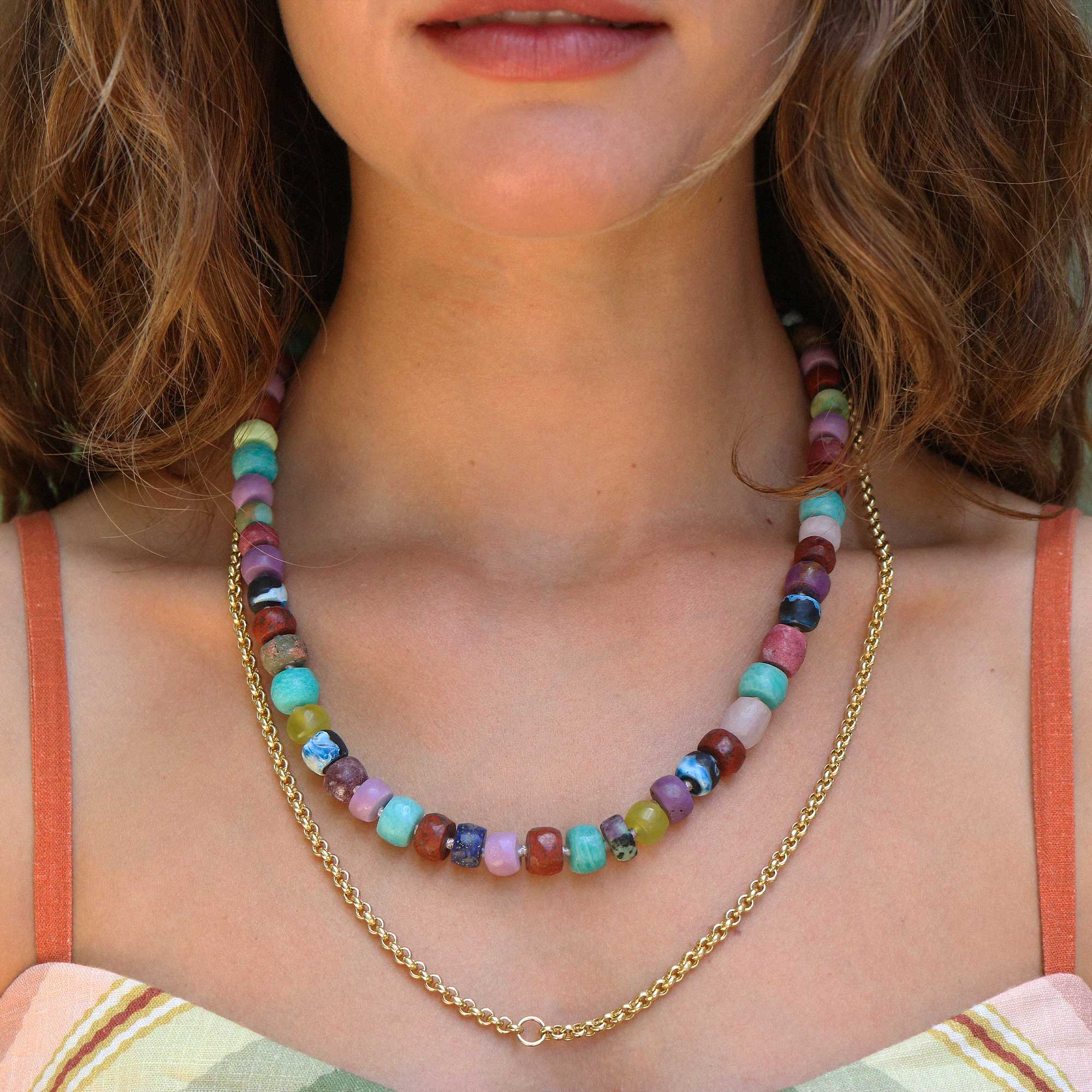 A close-up of a model wearing a double-strand necklace. The top strand features colorful, irregularly shaped beads in shades of pink, blue, green, purple, and brown.