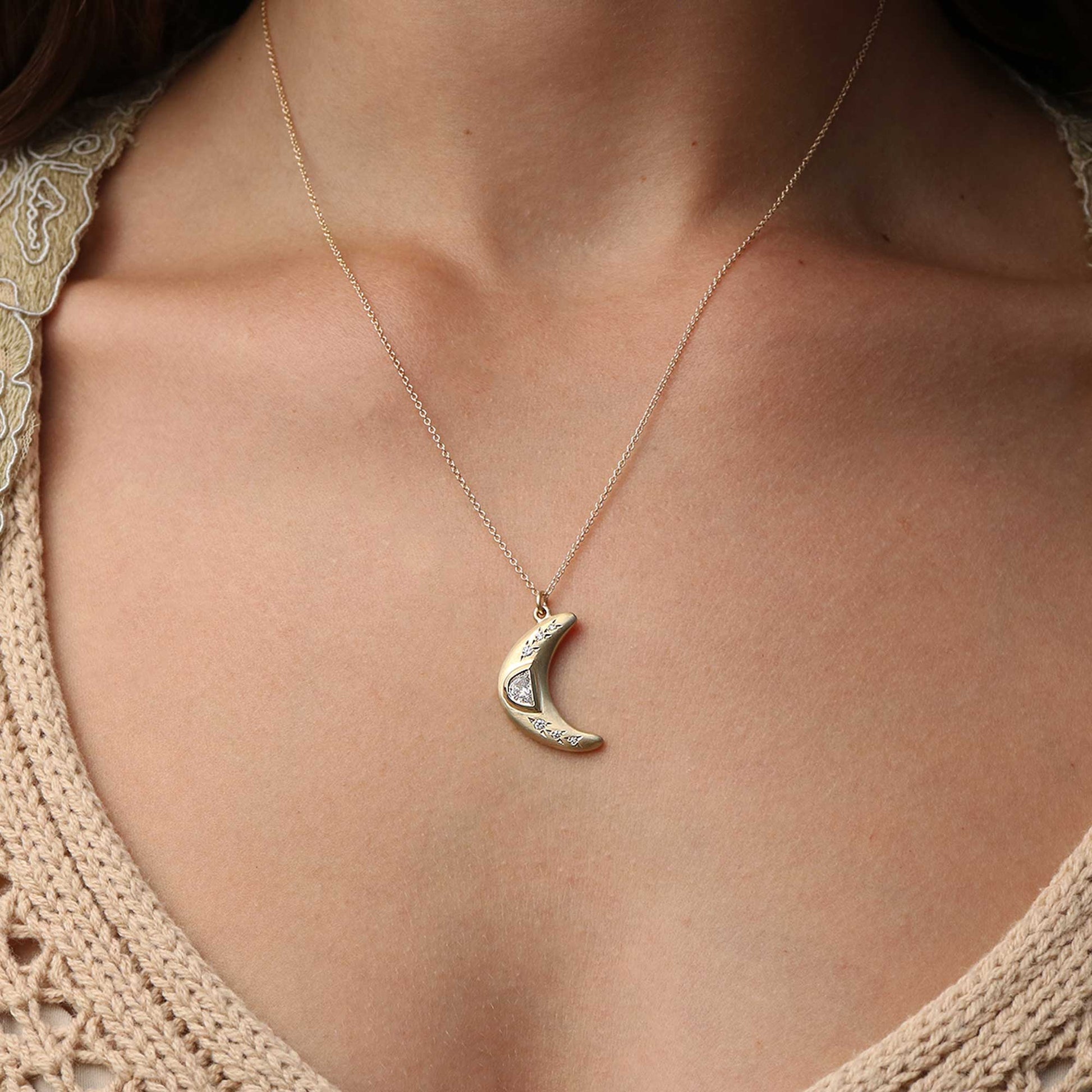 A gold crescent moon pendant necklace with a gold moonstone inlay, shown worn on a model's neck over a beige knit top.