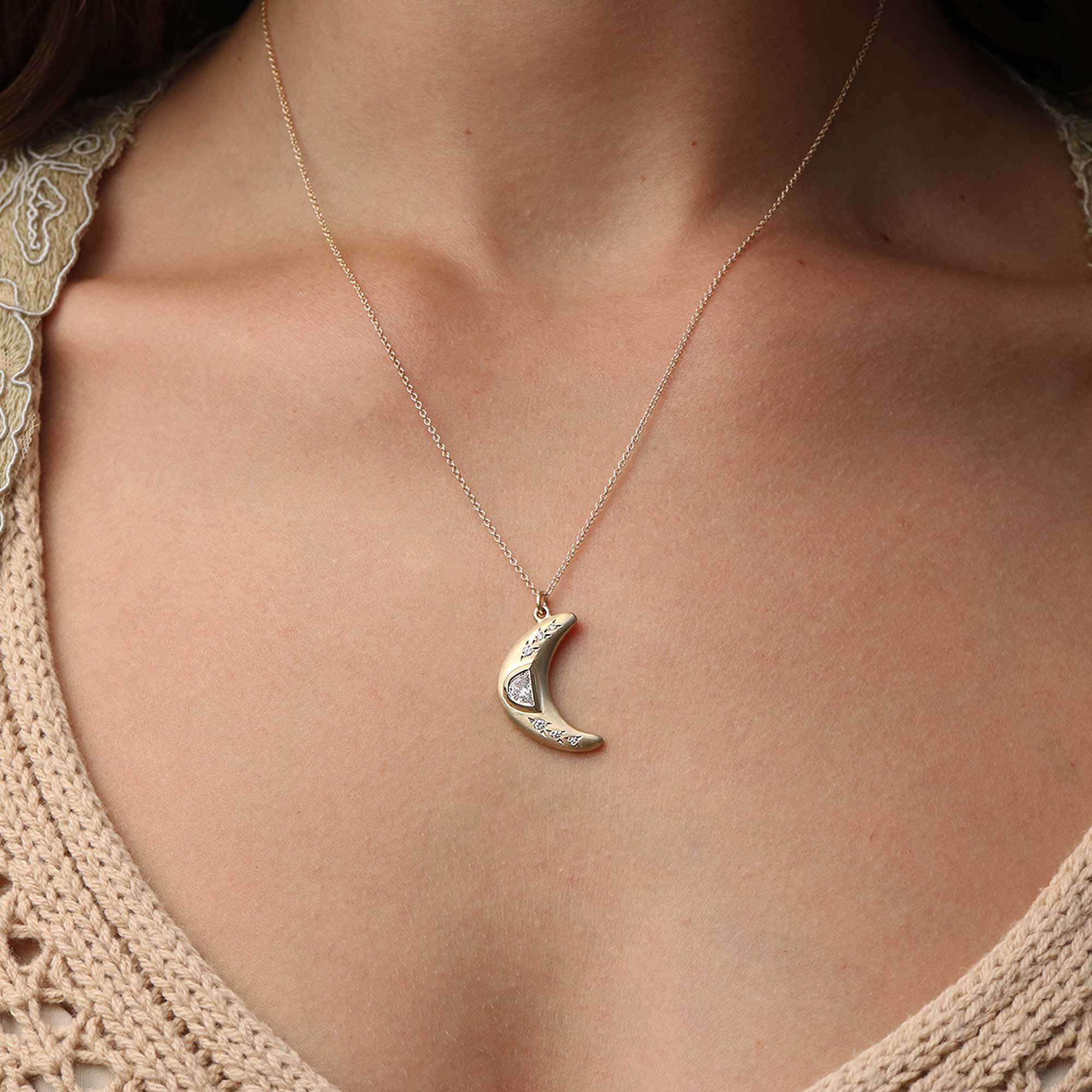 A gold crescent moon pendant necklace with a gold moonstone inlay, shown worn on a model's neck over a beige knit top.