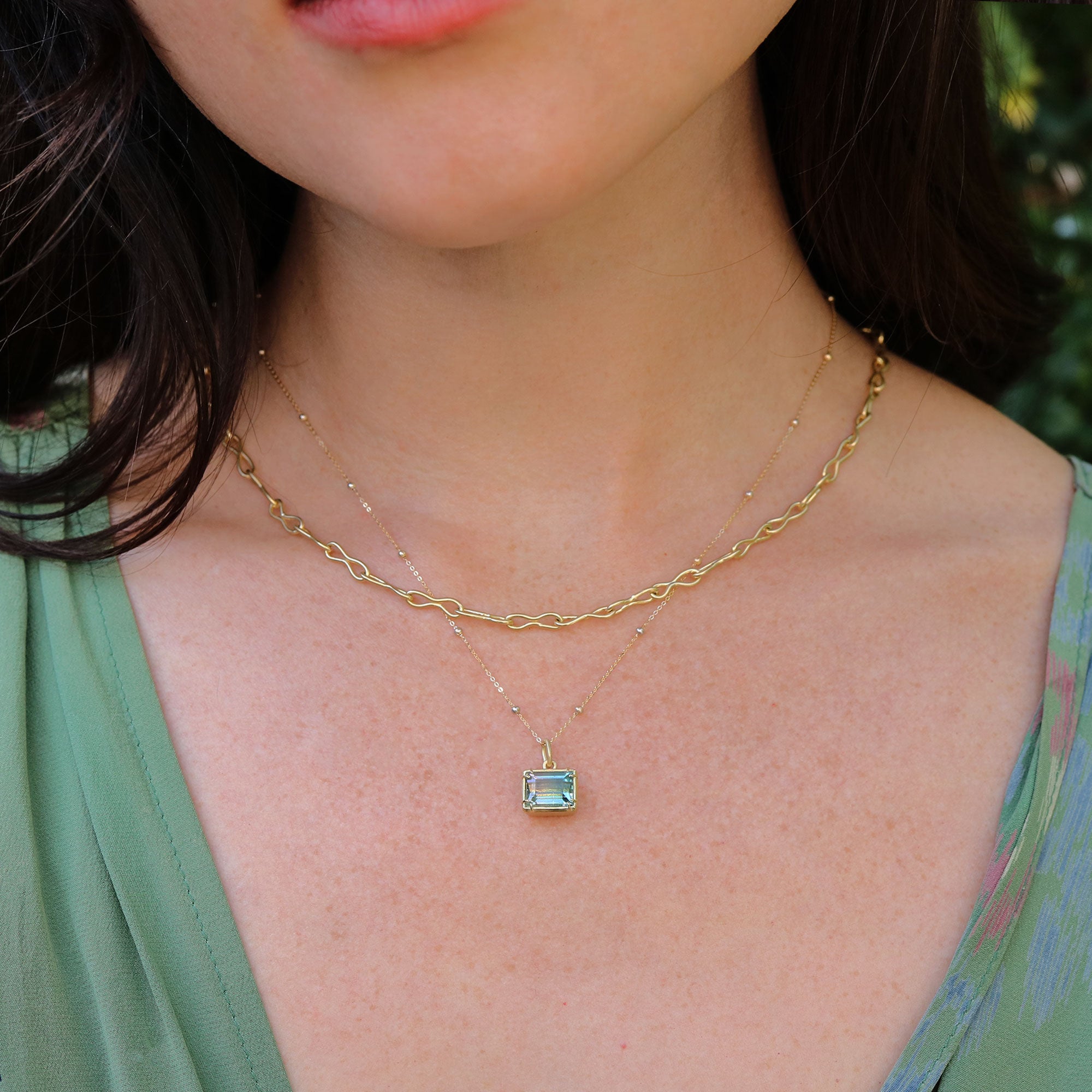 Gold necklace with a bicolor tourmaline gemstone pendant worn by a person