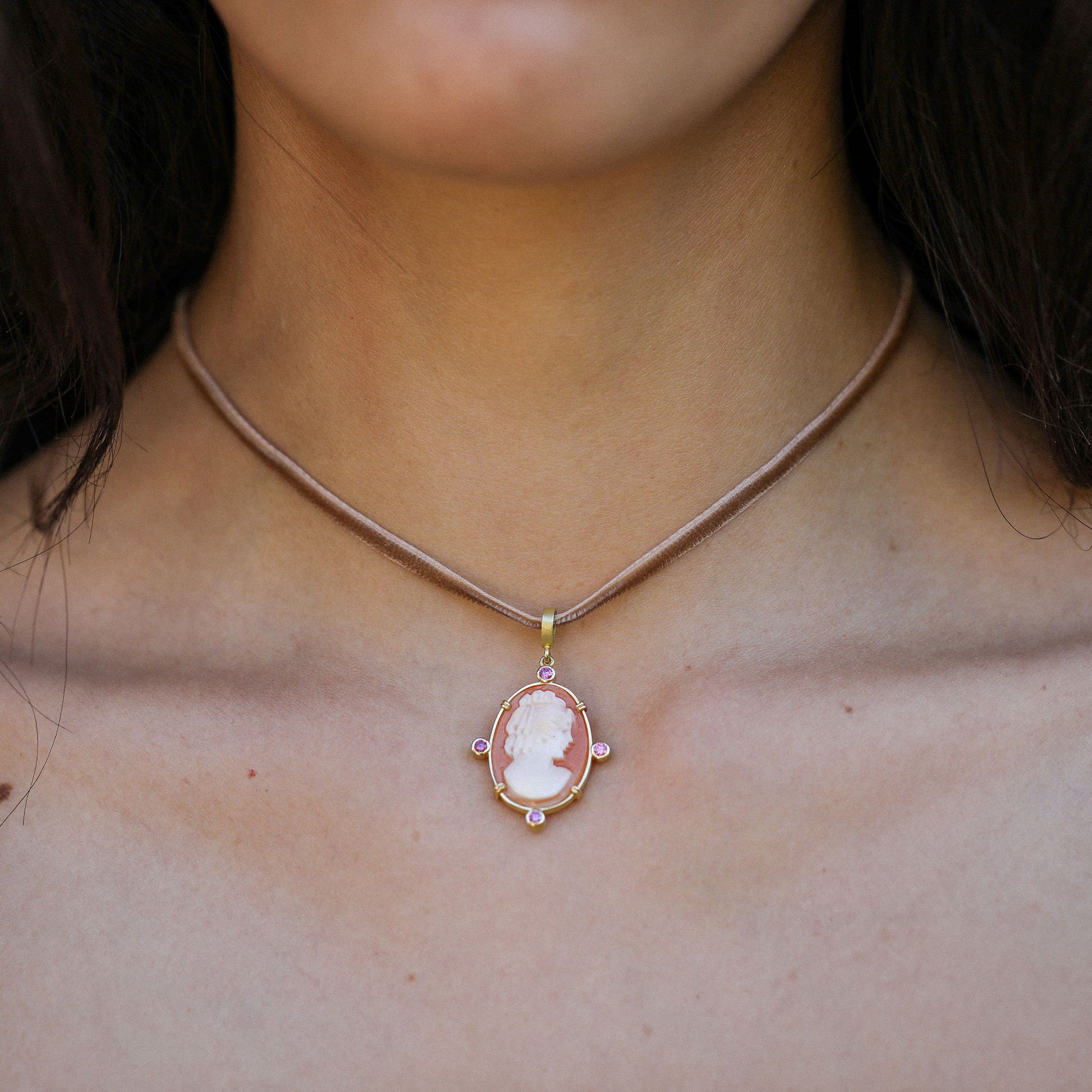 close up of a necklace on a velvet string with an 18k gold yellow pendant featuring a cameo shell and pink tourmaline by designer brooke gregson.