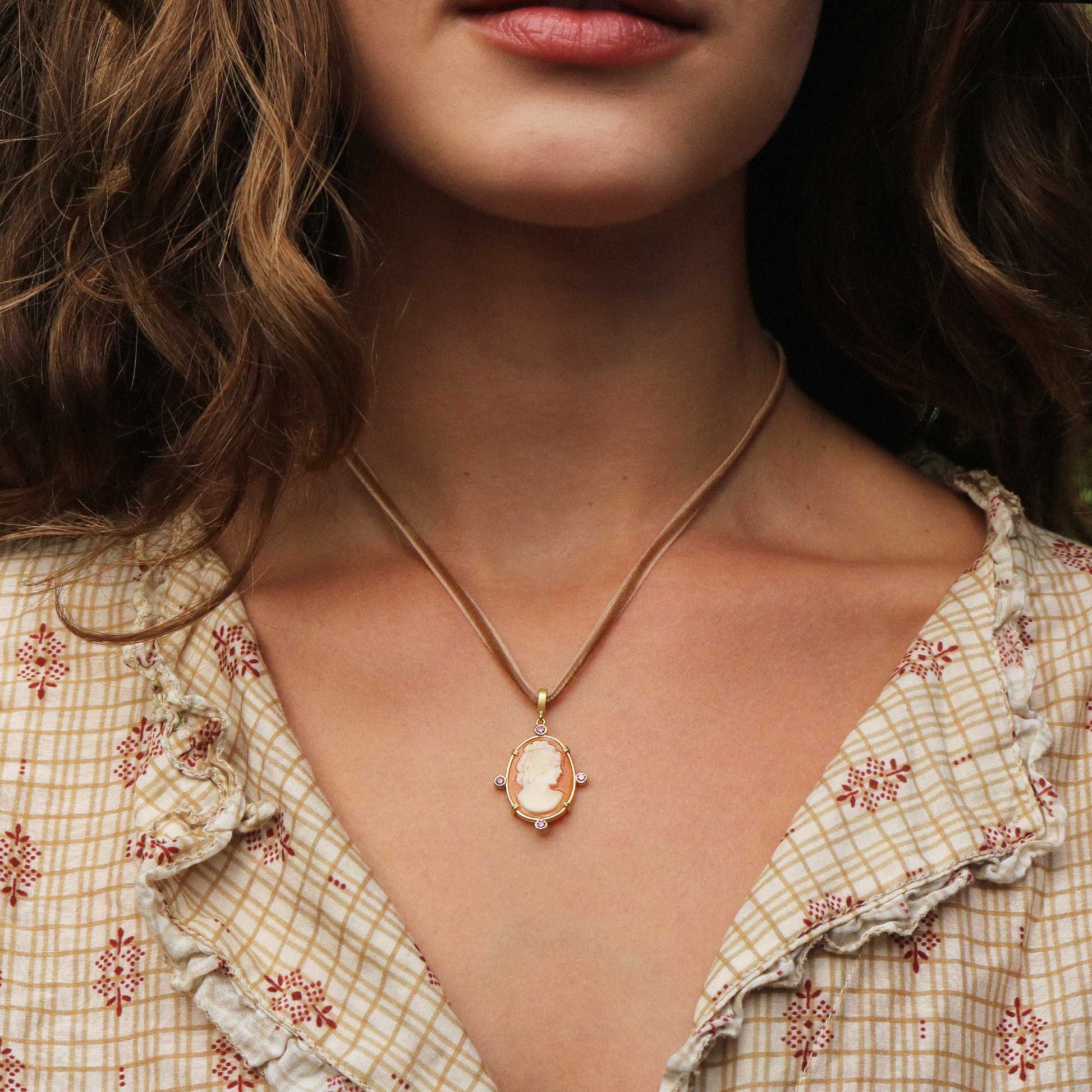 A close-up of a woman wearing a delicate gold chain necklace with an oval pendant featuring a classic cameo-style profile.