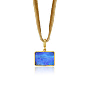 A gold pendant necklace featuring a rectangular blue opal stone with vibrant iridescent play-of-color, suspended from a textured gold snake chain against a white background.