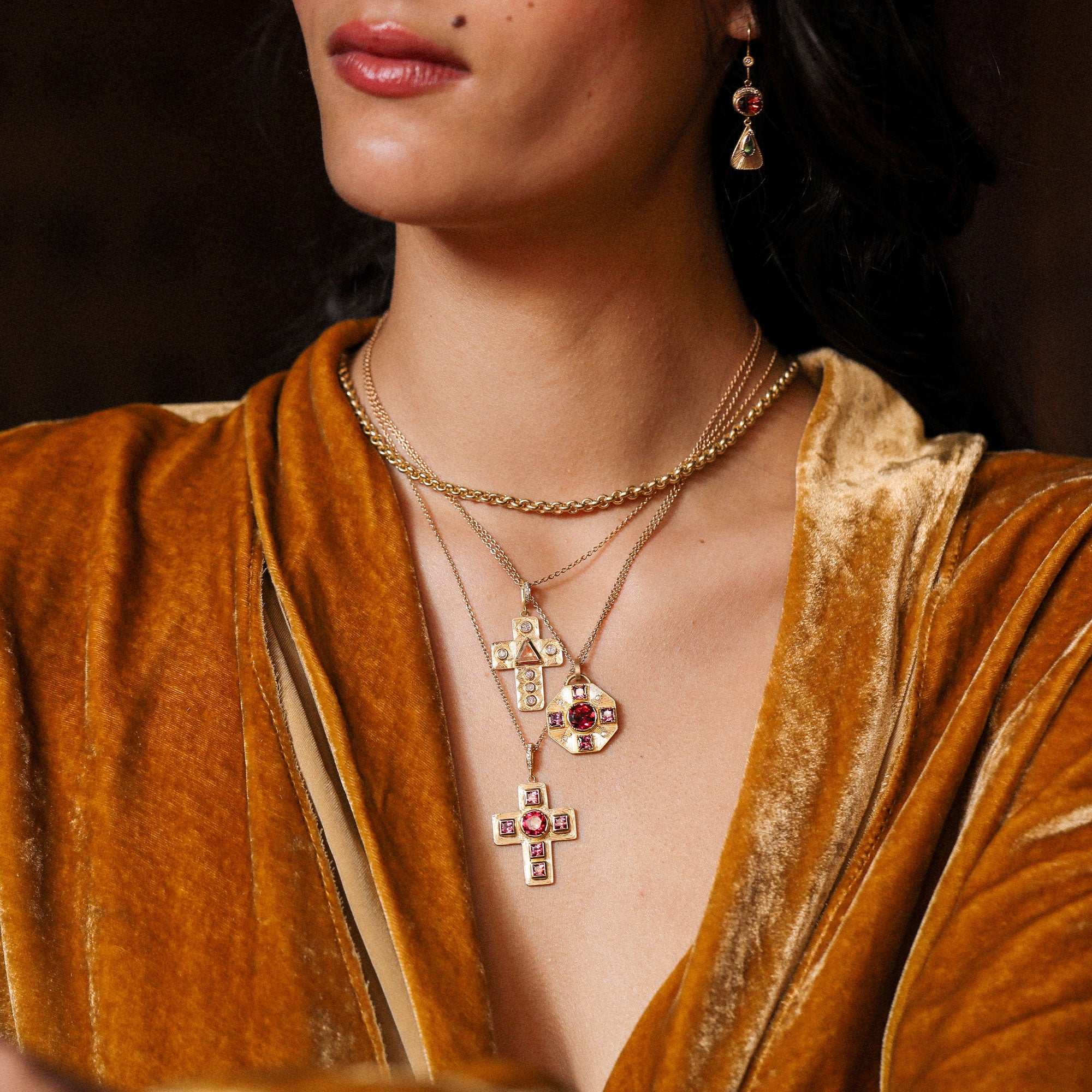Close-up of a person wearing gold jewelry with red ruby and garnet stones against a dark background