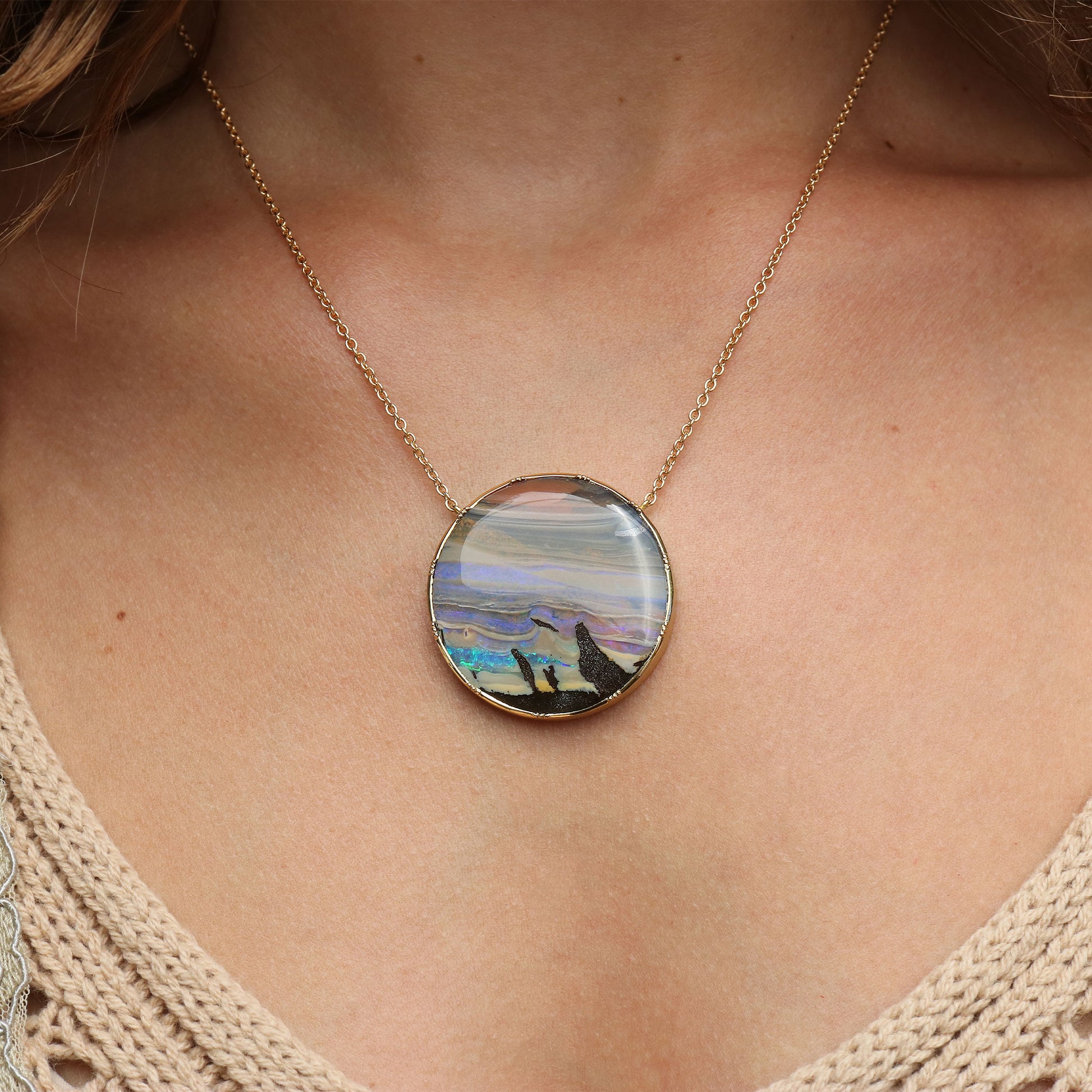A gold chain necklace with a round pendant featuring a colorful landscape opal, shown worn on a model's neck.