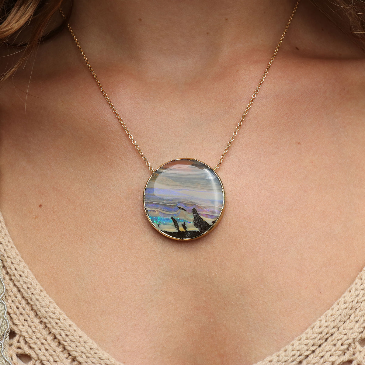 A gold chain necklace with a round pendant featuring a colorful landscape opal, shown worn on a model's neck.