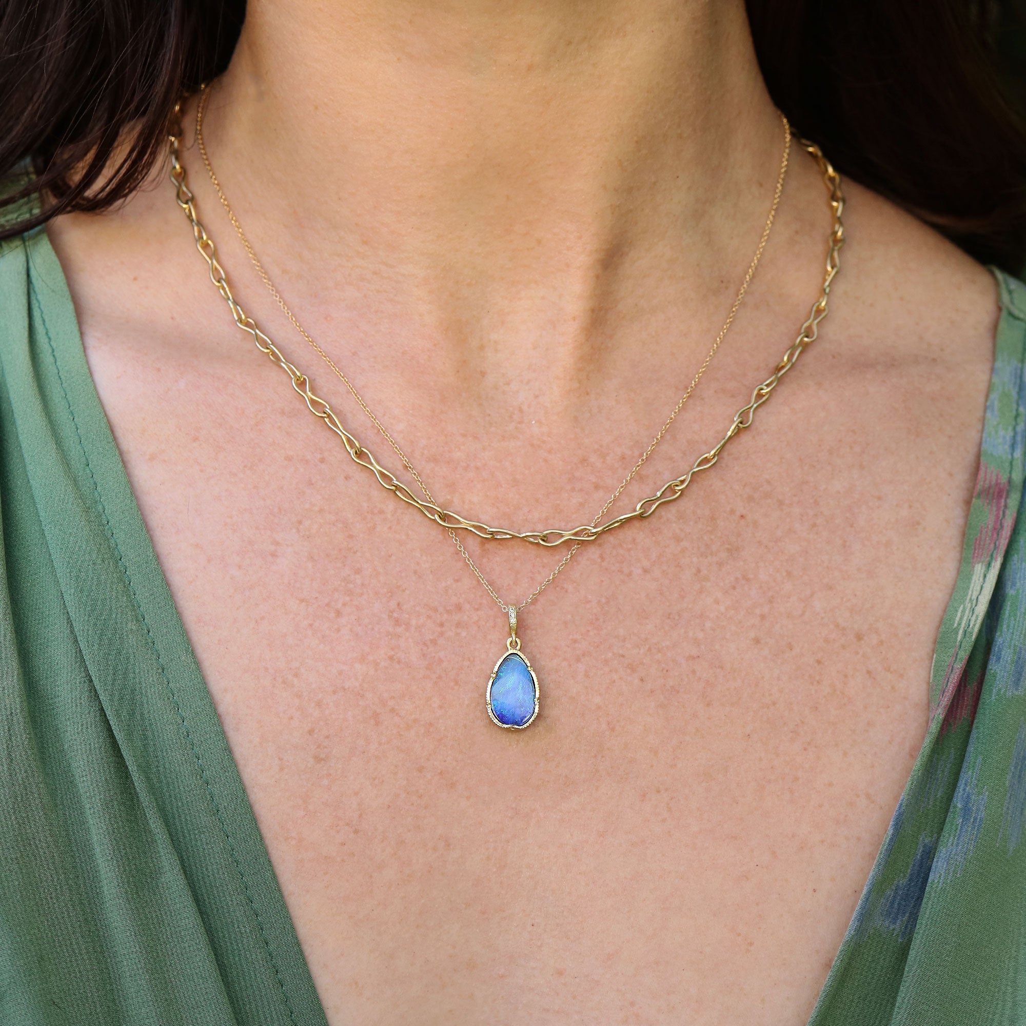 Gold necklace with a blue boulder opal pendant worn by a person in a green top.