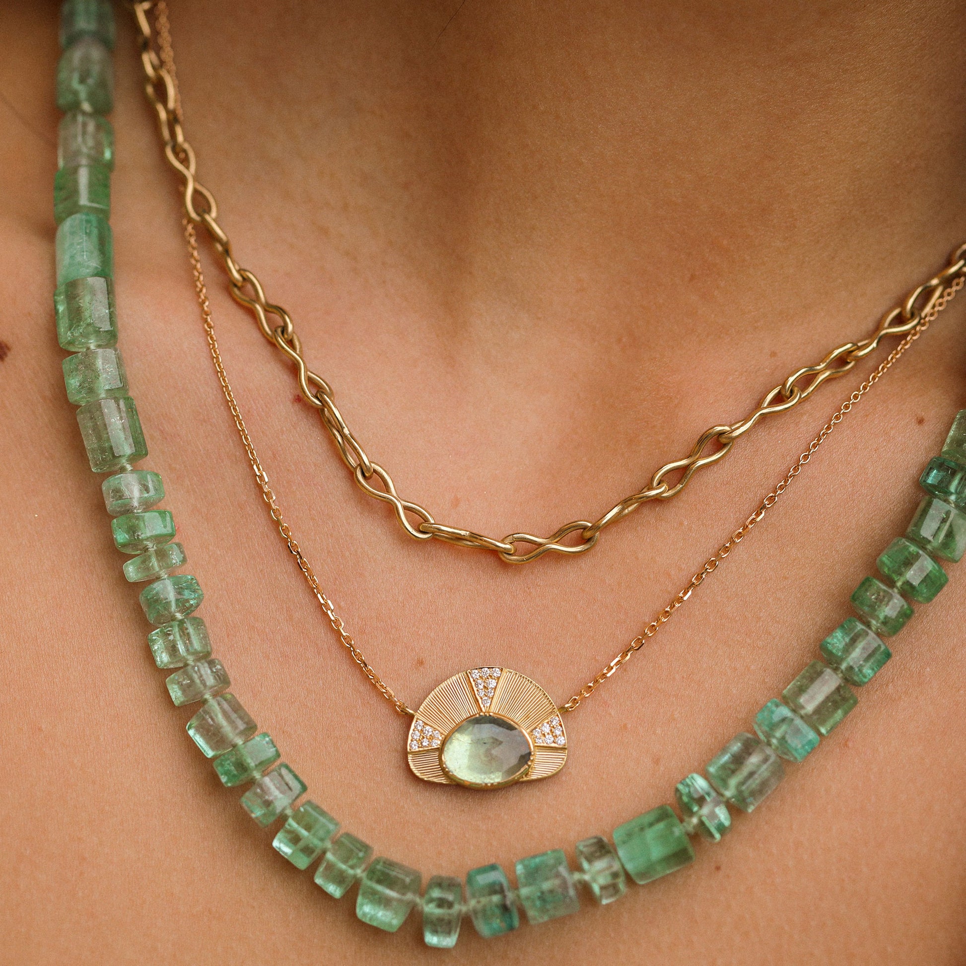Two necklaces on a person's neck: one green gemstone necklace and one gold chain.