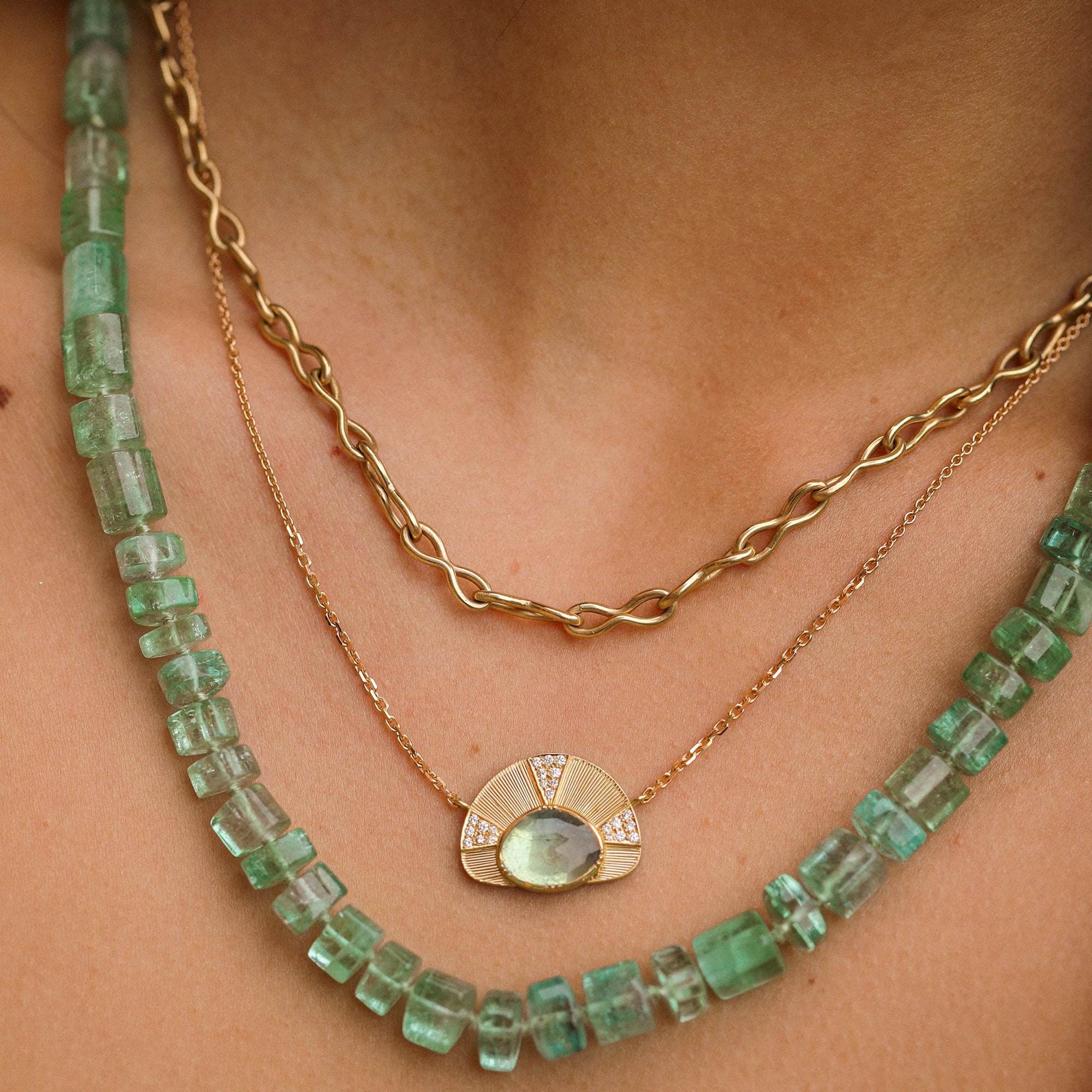 Two necklaces on a person's neck: one green gemstone necklace and one gold chain.