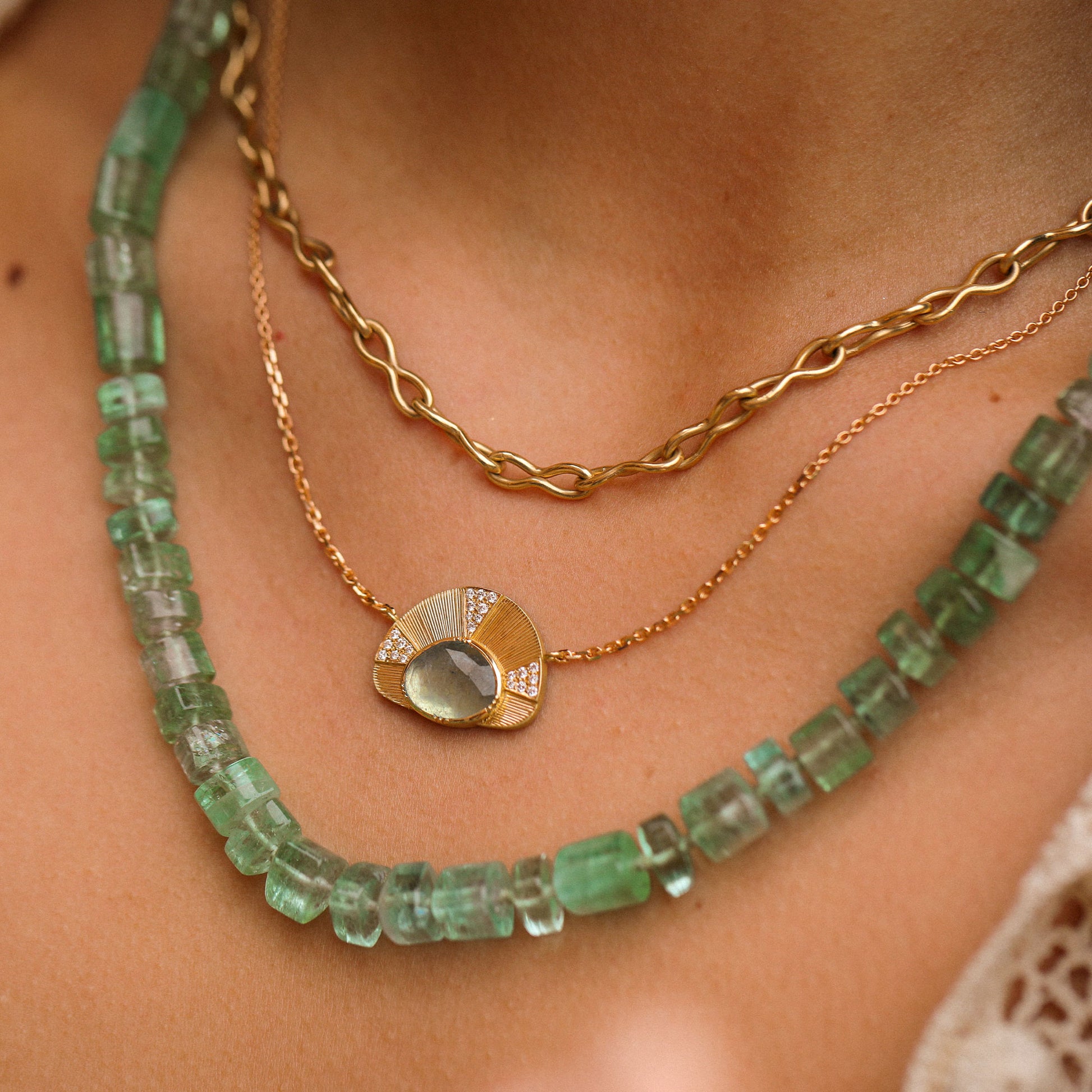 Close-up of a person wearing two necklaces: one green beaded and one gold chain with a pendant.