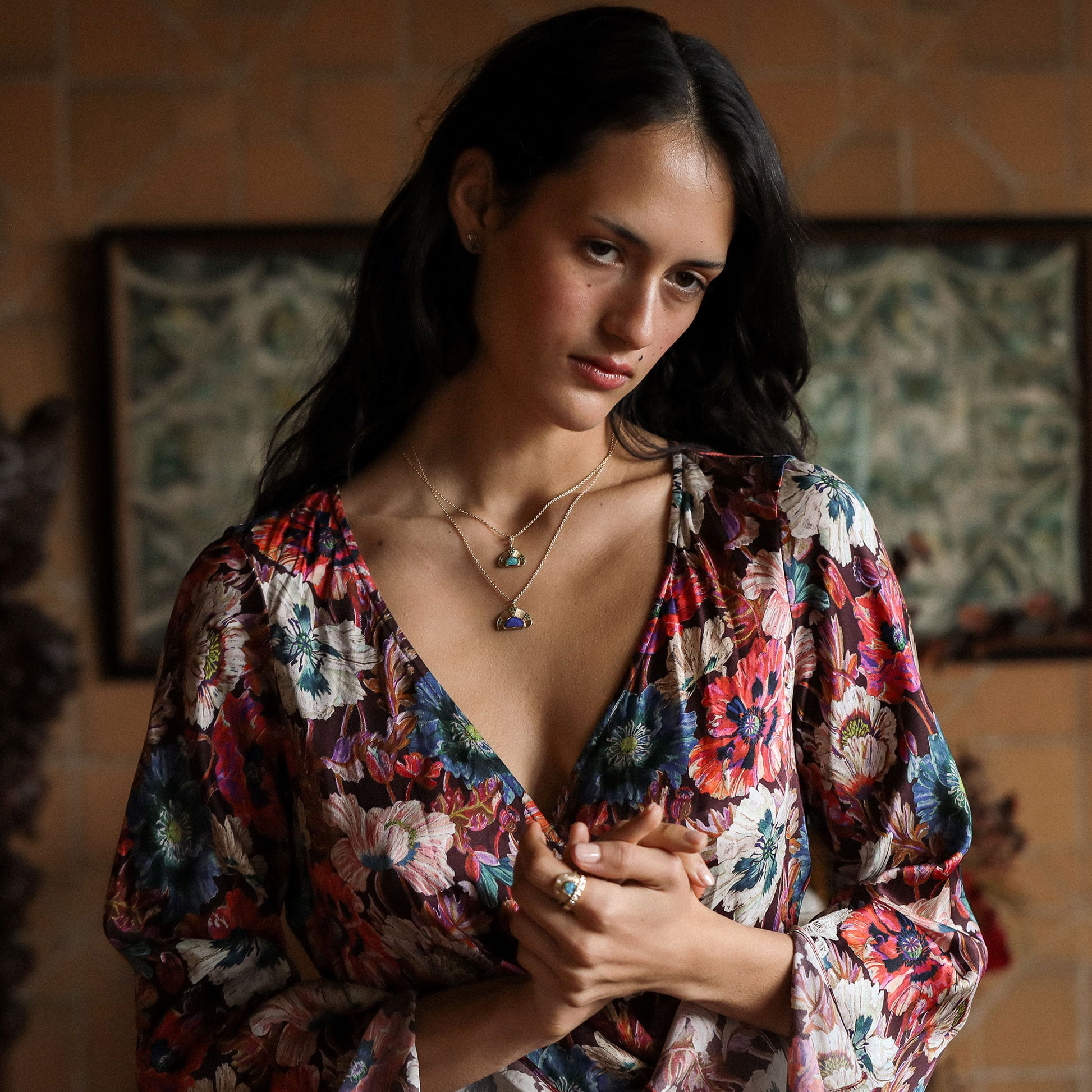 Woman wearing a colorful floral dress with a patterned background and opal necklaces on inn 18k gold.