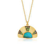 An 18k yellow gold pendant necklace featuring a fan-shaped design with a central iridescent blue-green opal and small emerald and sapphire gemstone accents with hand engraving, shown on a white background with a soft reflection. By jewelry designer Brooke Gregson.