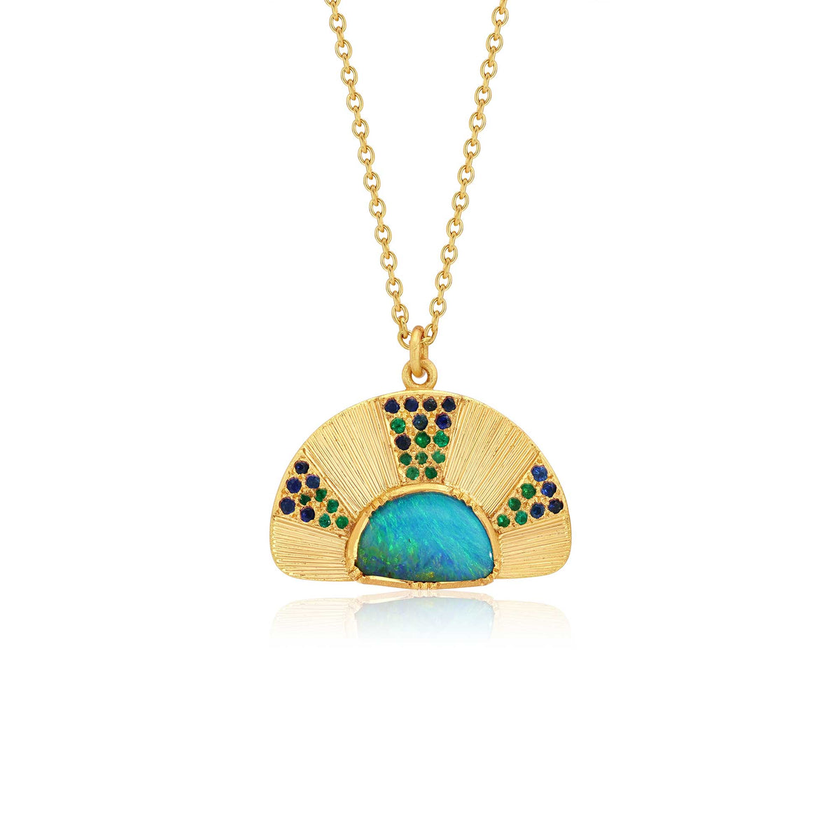An 18k yellow gold pendant necklace featuring a fan-shaped design with a central iridescent blue-green opal and small emerald and sapphire gemstone accents with hand engraving, shown on a white background with a soft reflection. By jewelry designer Brooke Gregson.
