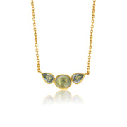 A gold chain necklace featuring a pendant with three teardrop-shaped light blue-green sappphire gemstones in a gold bezel setting, displayed against a white background with a soft reflection below.