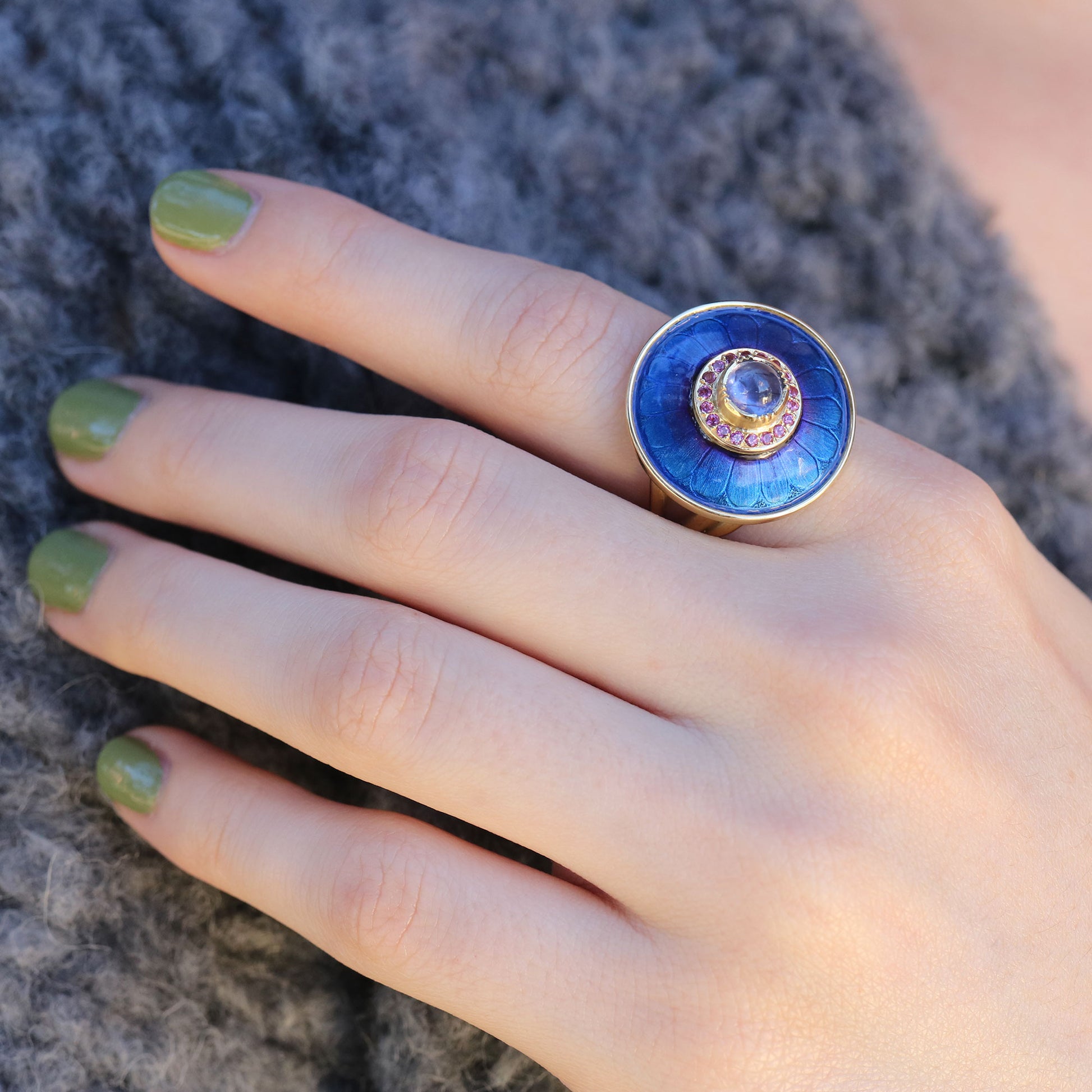 Hand wearing a blue ring with a sapphire gemstone on a textured gray background