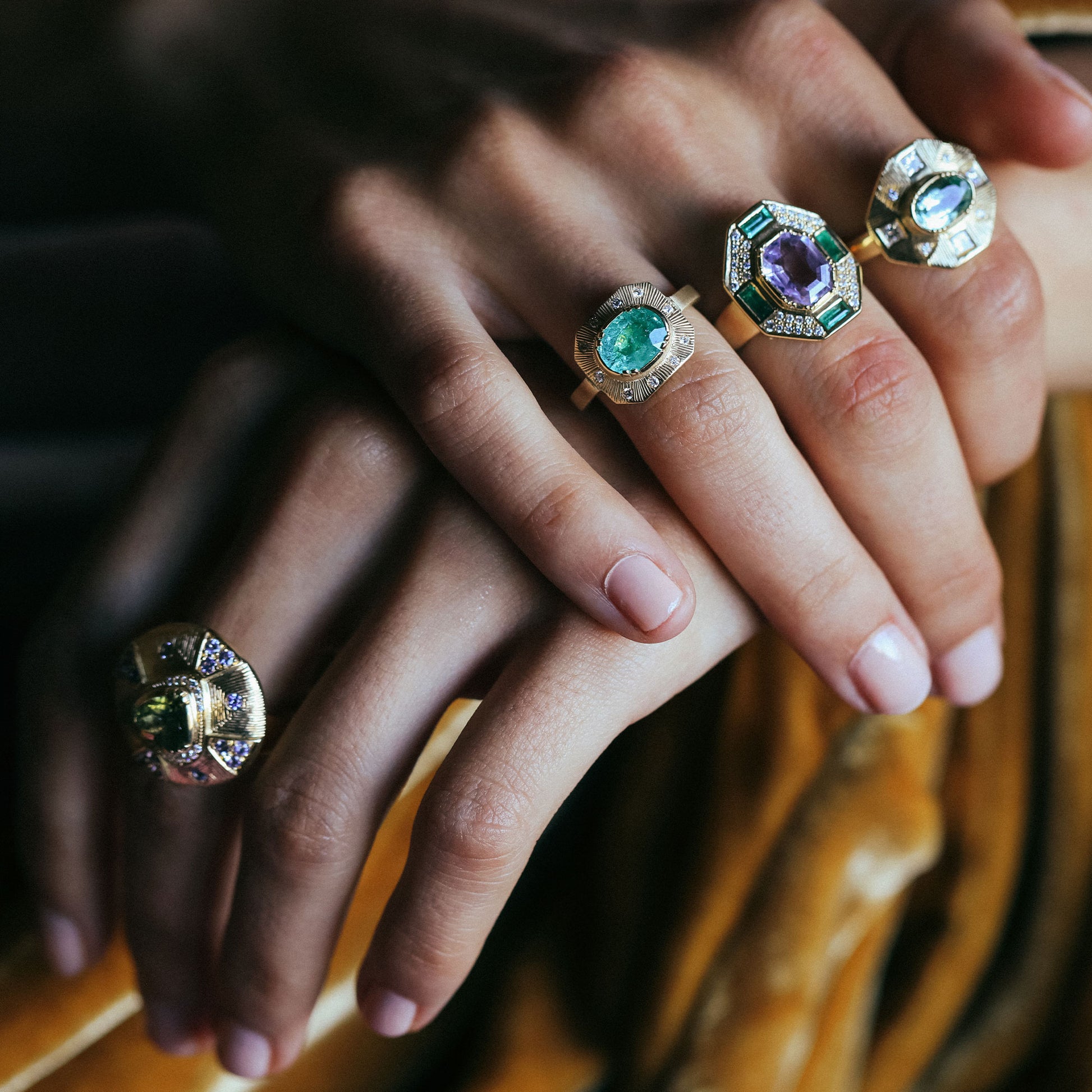 Close-up of hands wearing gold rings with gemstones on a blurred background