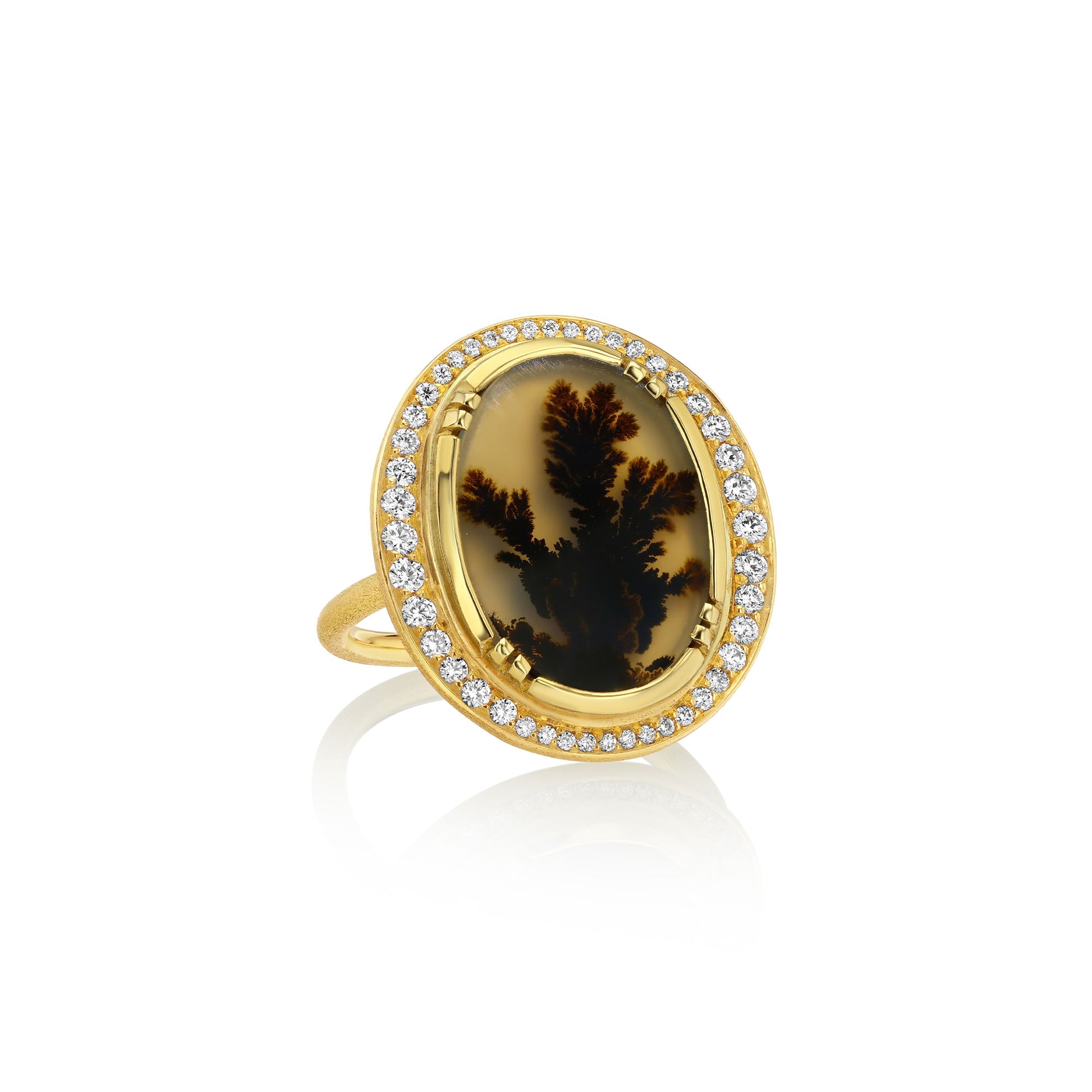 An 18k gold ring featuring an oval dendritic agate stone with a dark brown to black dendritic pattern, surrounded by a halo of small white diamond stones, set against a plain white background with a soft reflection.