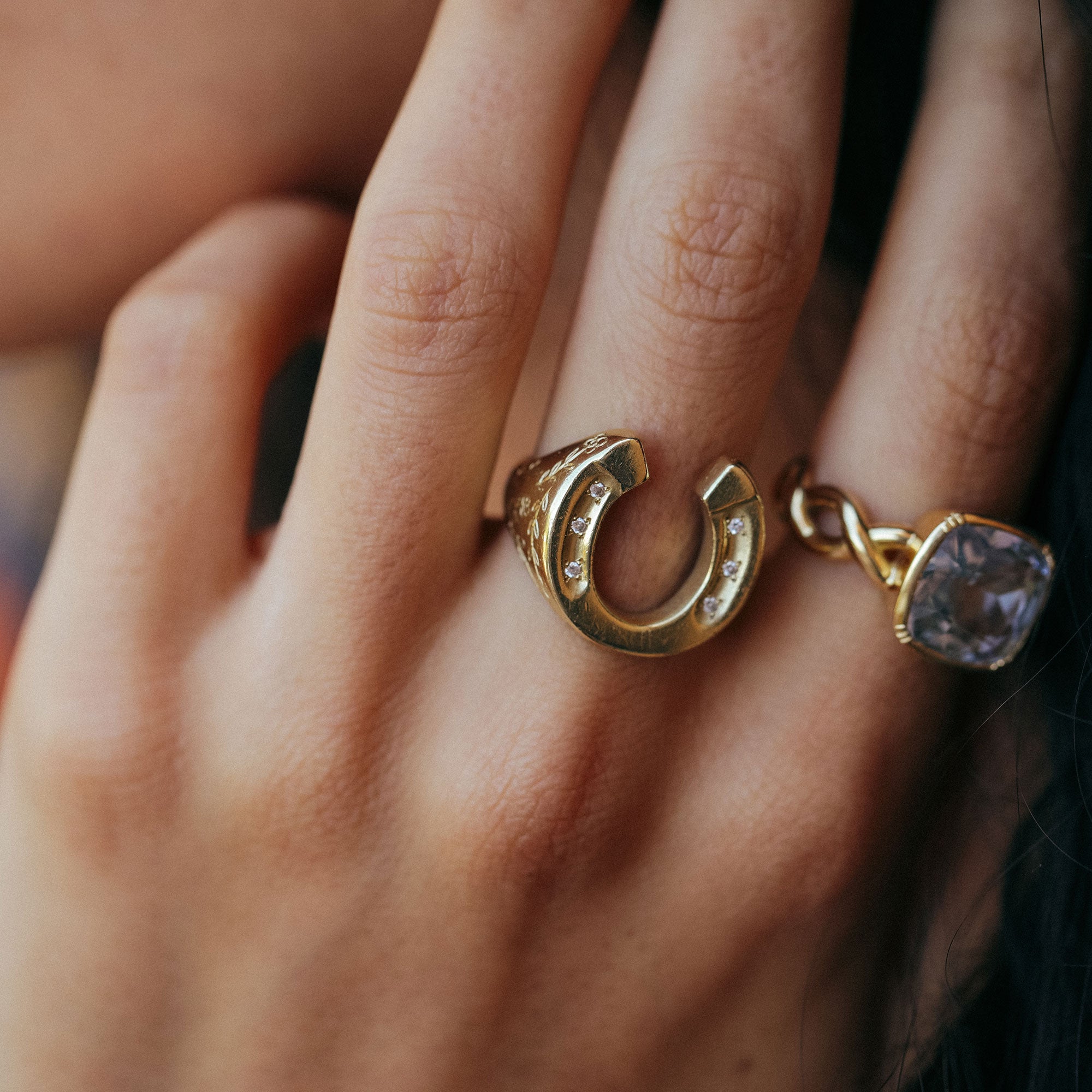 close up of hand wearing horseshoe ring with white diamonds and hand engraved detailing.