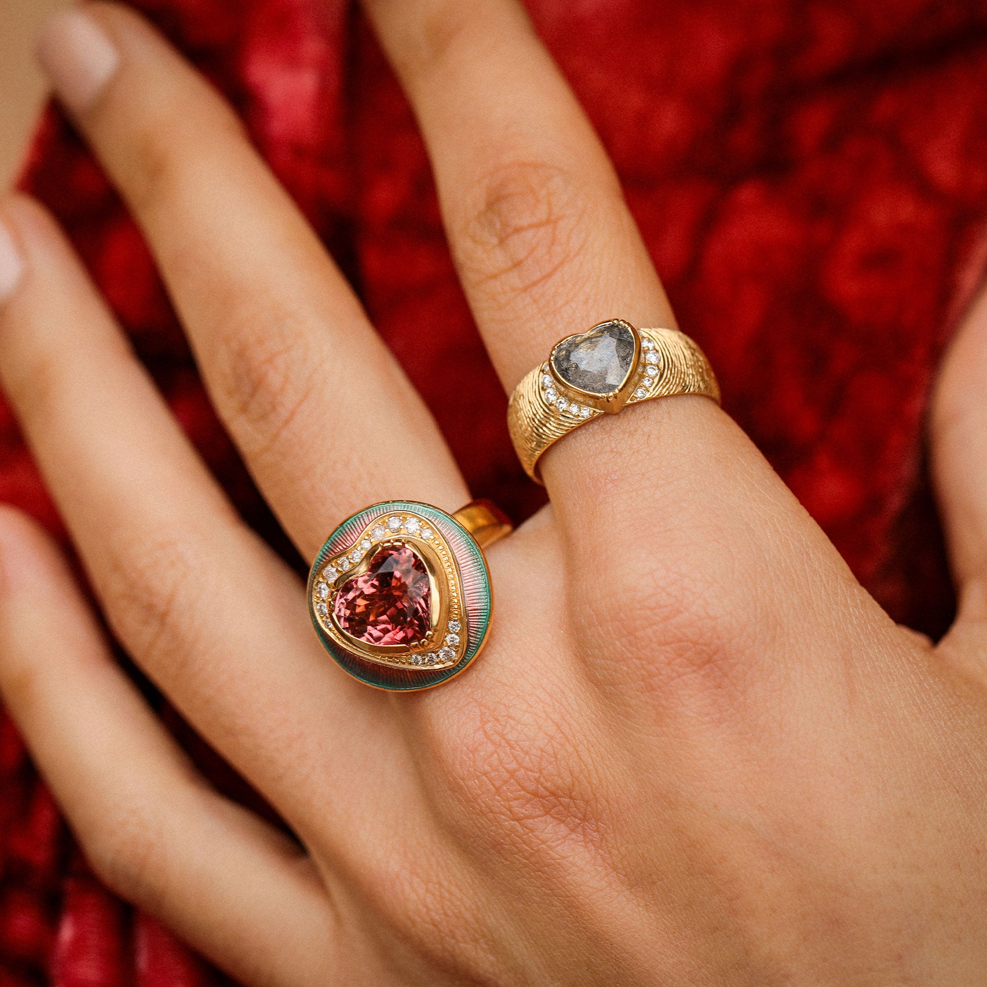 Close-up of a hand wearing two gold rings with gemstones against a red fabric background