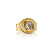 18k gold ring with a large central raw diamond cabochon stone and smaller pink diamond stones around on a white background.
