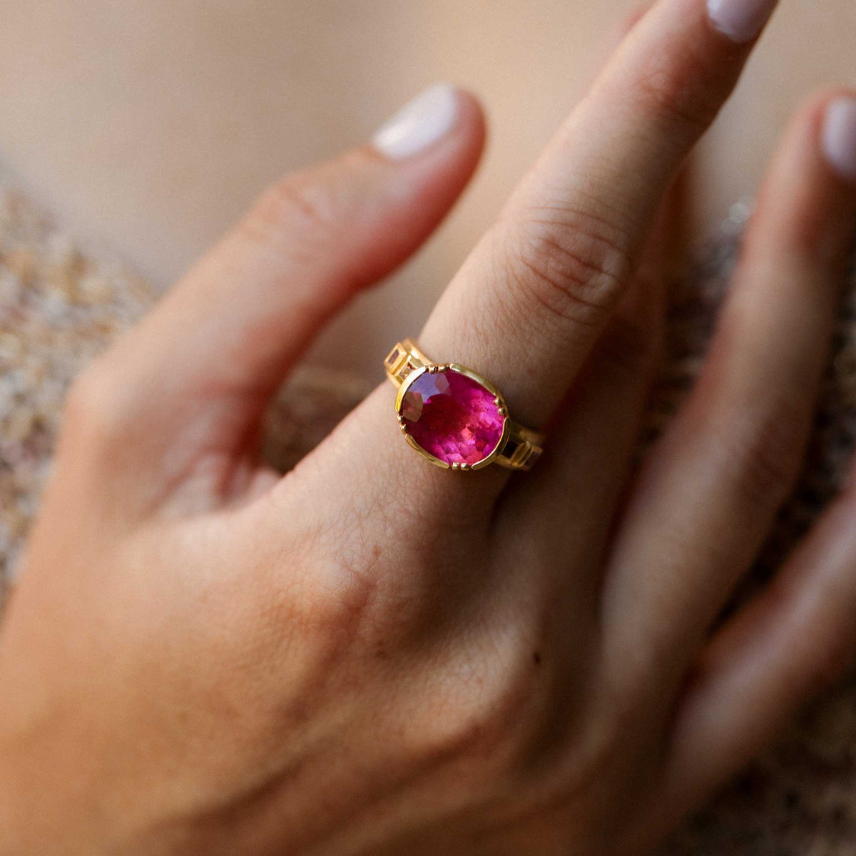 A gold ring with a large oval pink tourmaline gemstone worn on a person's ring finger, shown in a close-up shot.