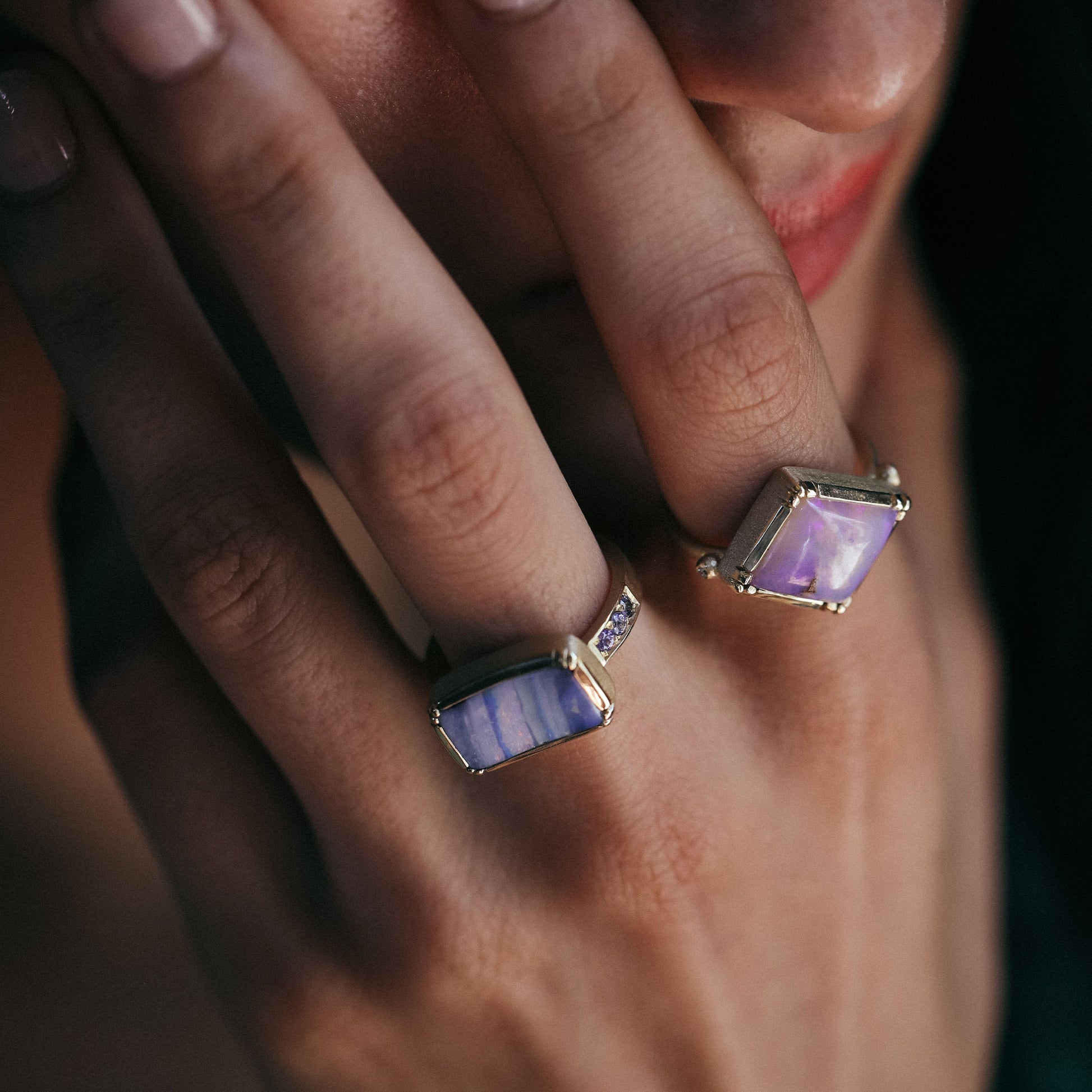 Close-up of a hand wearing two rings with purple gemstones on a blurred background