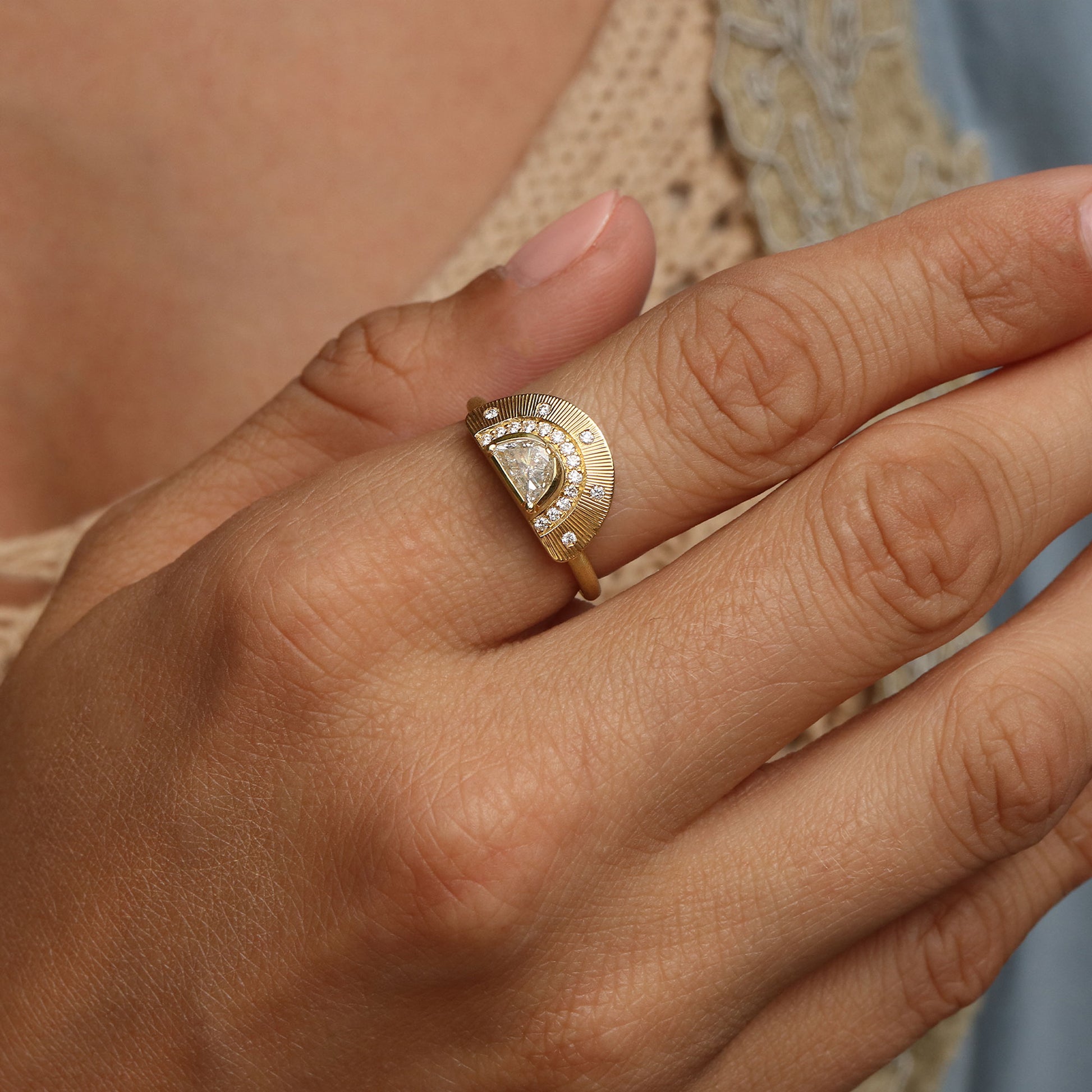 A close-up of a hand wearing a gold ring with a crescent-shaped setting, featuring a central clear gemstone surrounded by small accent stones.