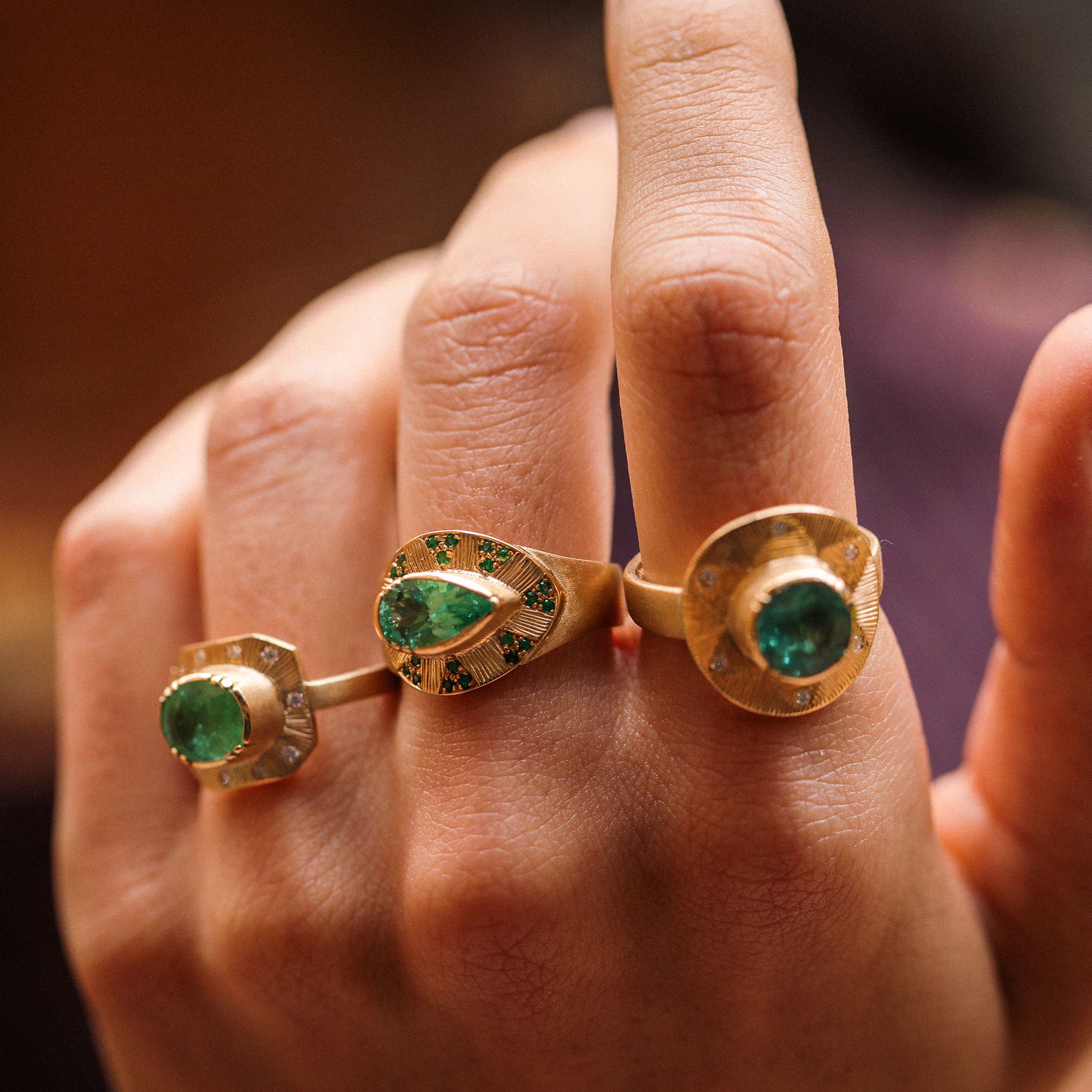 Gold rings with green gemstones on a person's finger against a blurred background