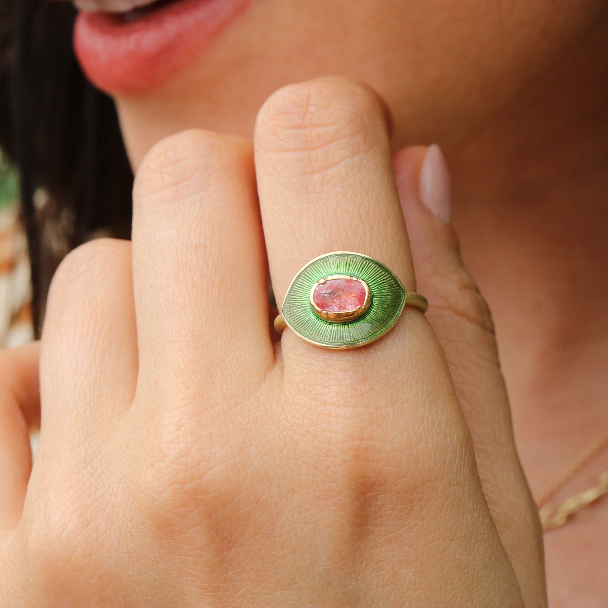 Close-up of a hand wearing a green enameled ring with a pink sapphire gemstone.