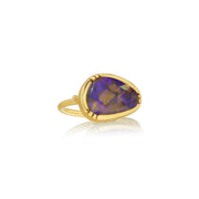 A gold ring featuring a teardrop-shaped purple opal stone with natural brown and blue flashes, set in a polished gold bezel on a white background with a soft reflection.