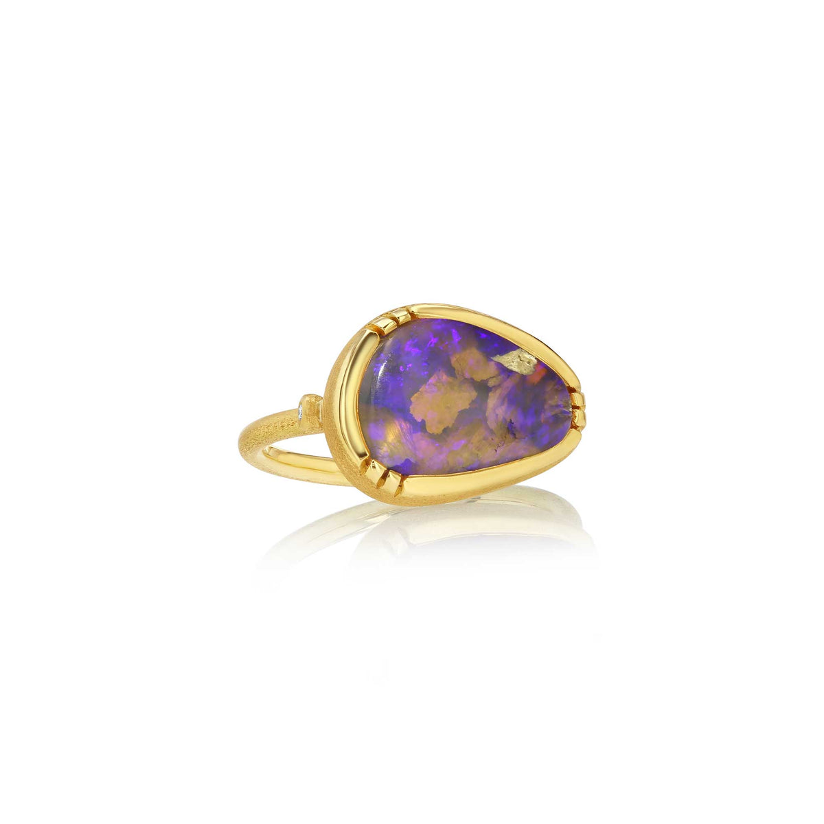A gold ring featuring a teardrop-shaped purple opal stone with natural brown and blue flashes, set in a polished gold bezel on a white background with a soft reflection.