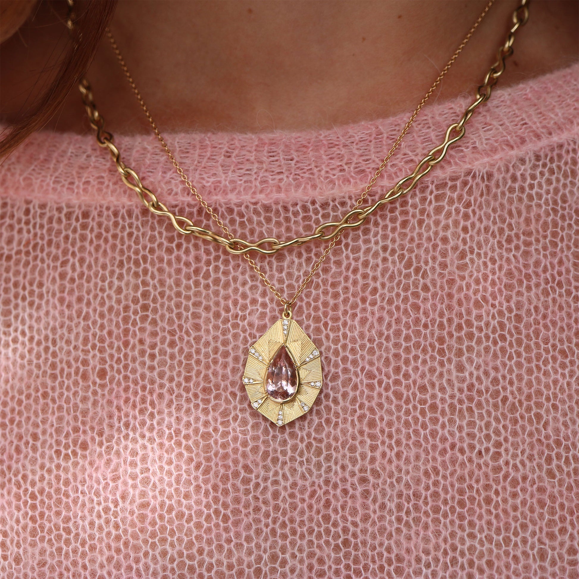 Gold necklace with a teardrop pendant on a pink textured fabric background